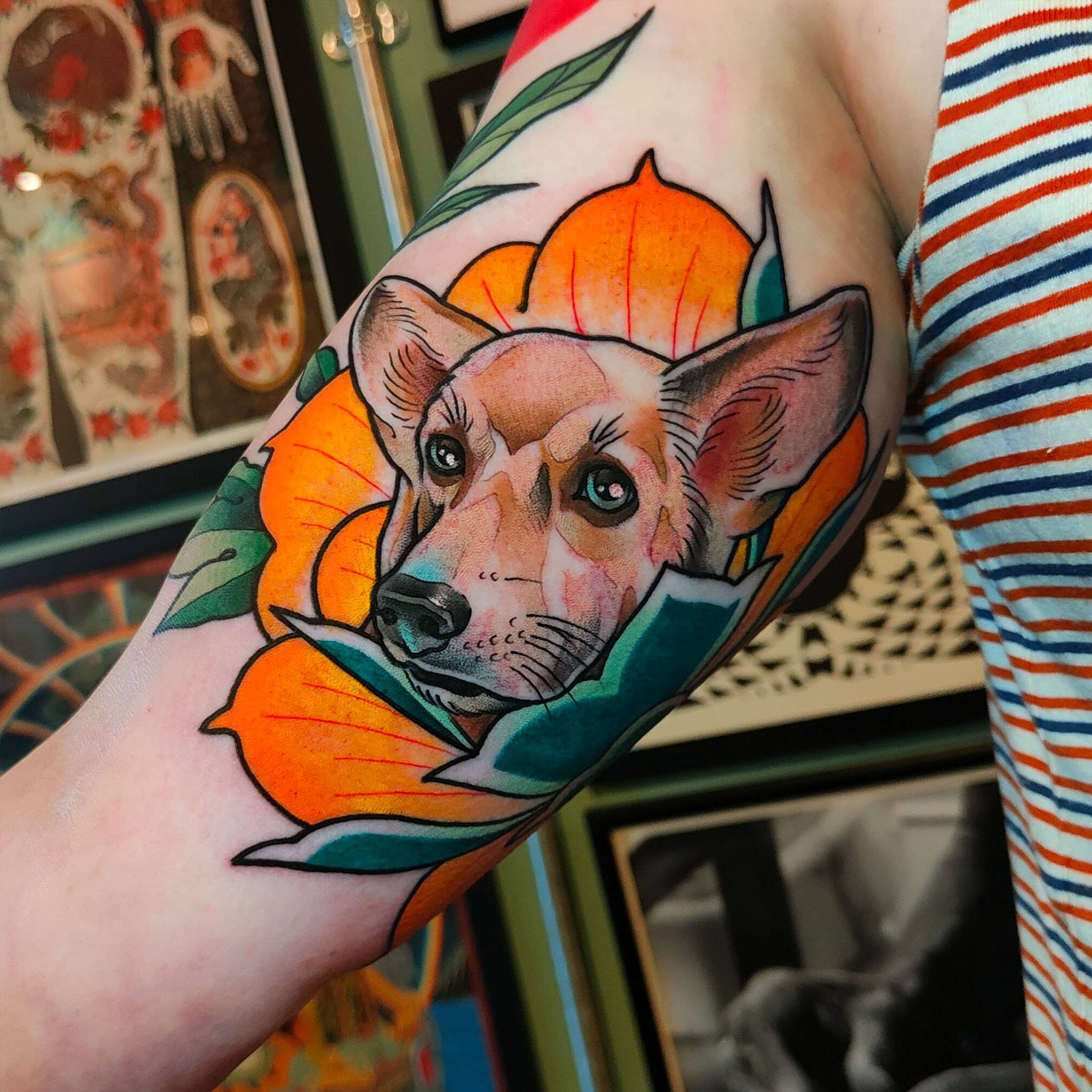 Tattoo of a dog's face framed by an orange flower on a person's arm.