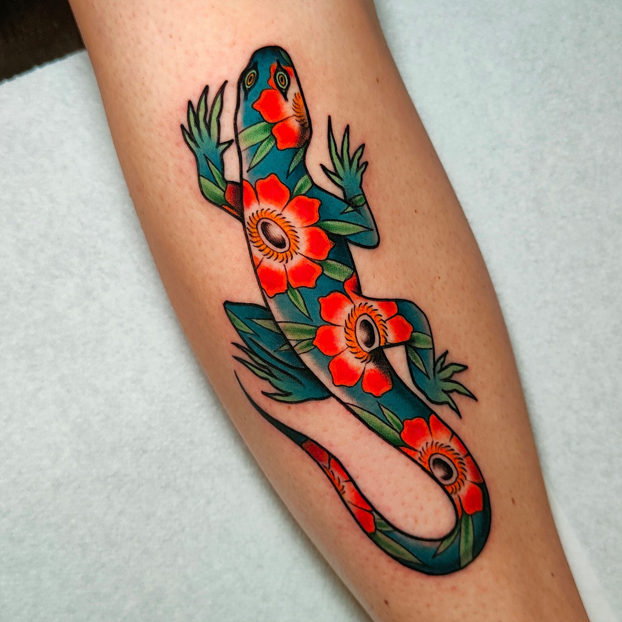 Tattoo of a colorful lizard with floral patterns on skin.