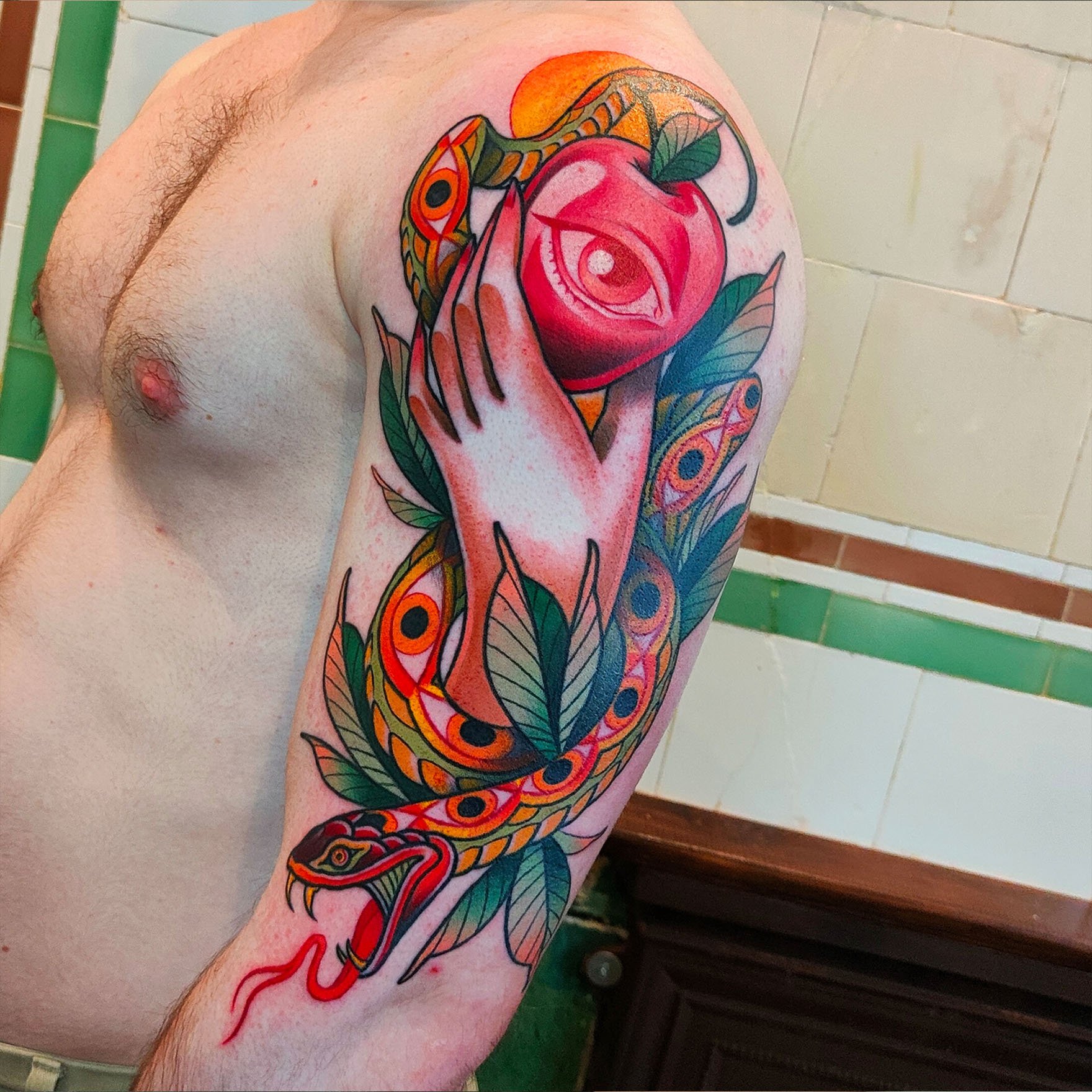Tattoo on a person's arm featuring a colorful design with a snake, apple with an eye, and leaves.