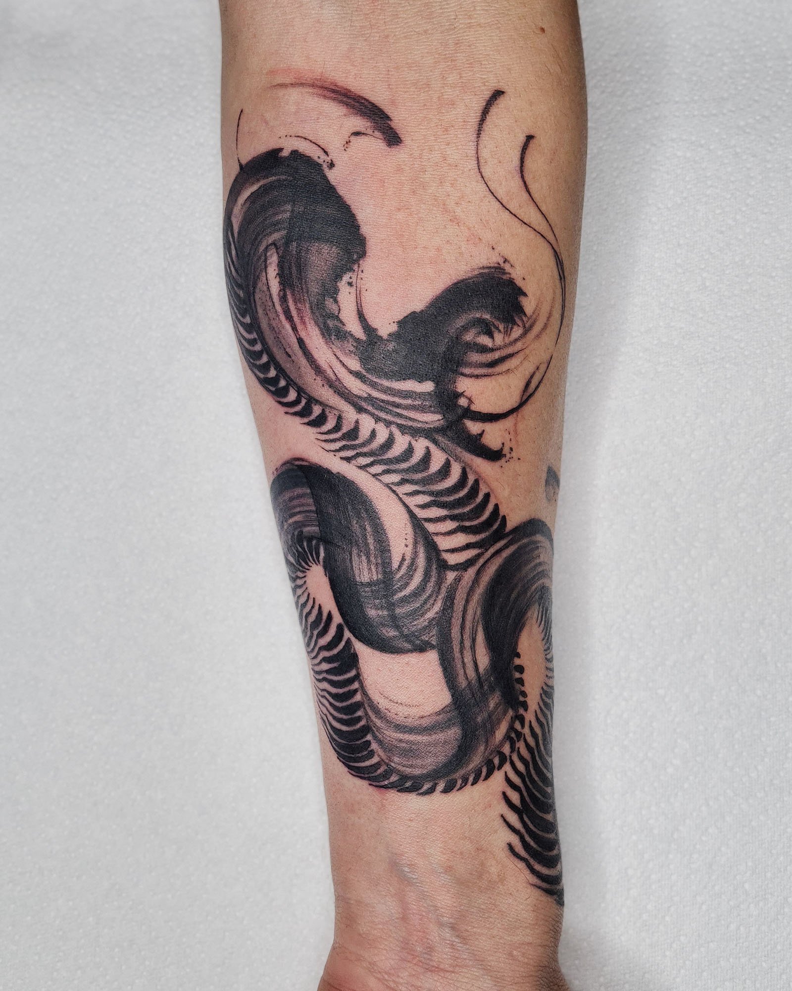 Abstract black ink snake tattoo with swirling and wavy patterns on forearm.