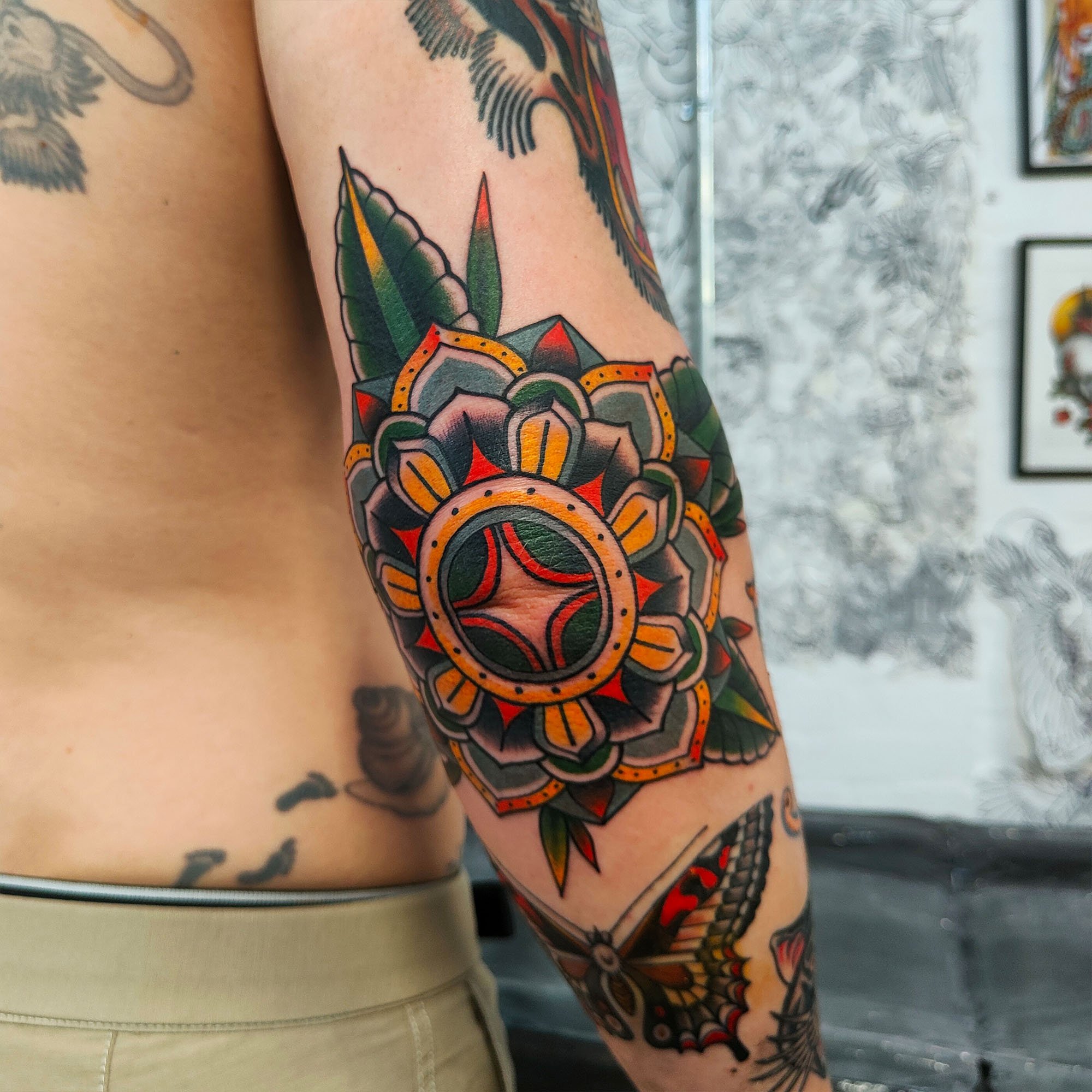 Colorful geometric tattoo on a person's upper arm, featuring circular and leaf elements, with black, green, yellow, and red hues.