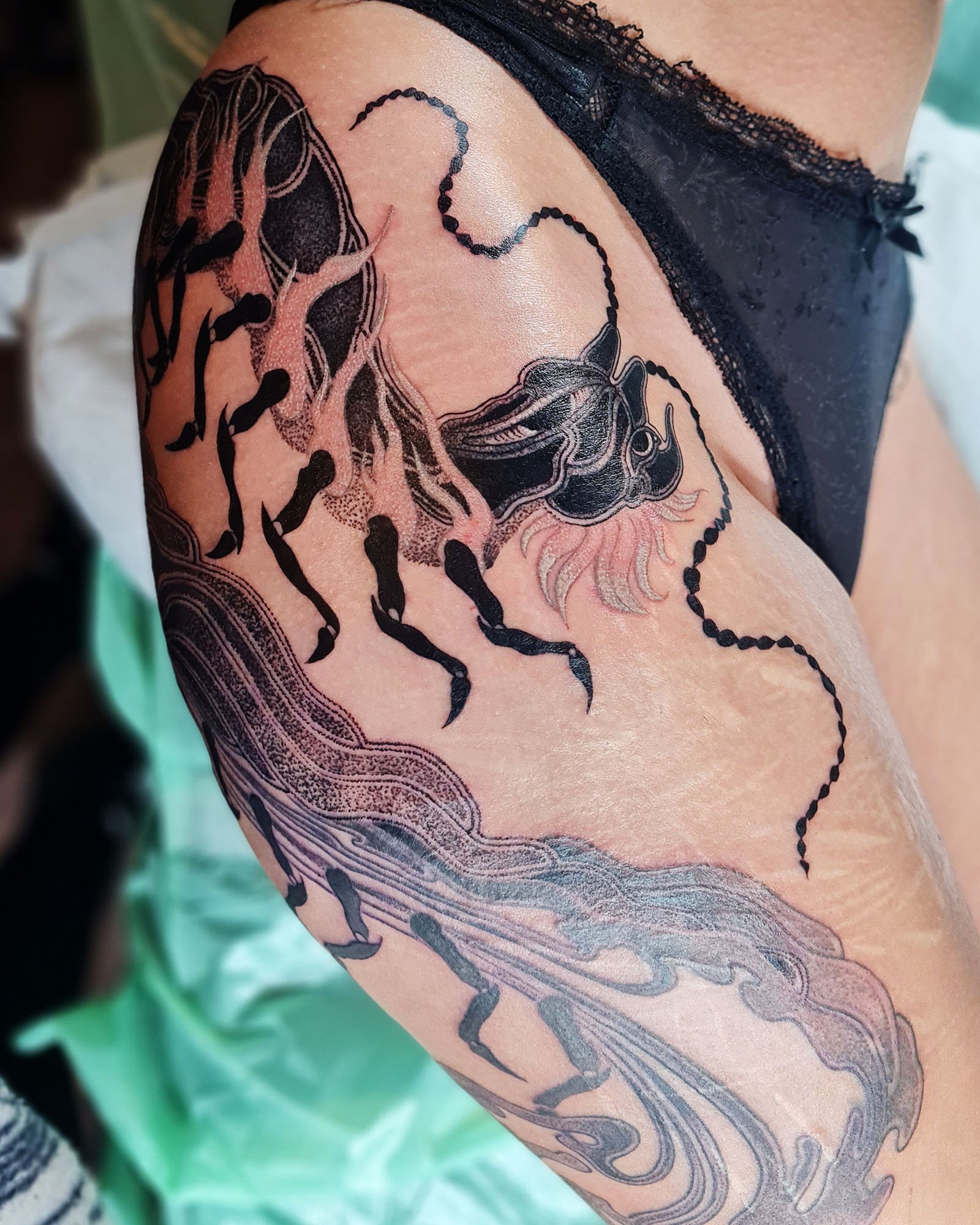 Detailed black and grey tattoo of an abstract centipede on the upper thigh