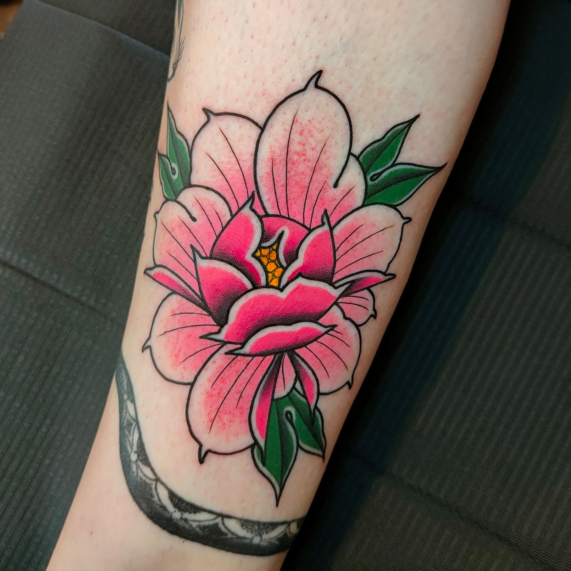 Colourful peony flower tattoo with pink petals and green leaves on skin.