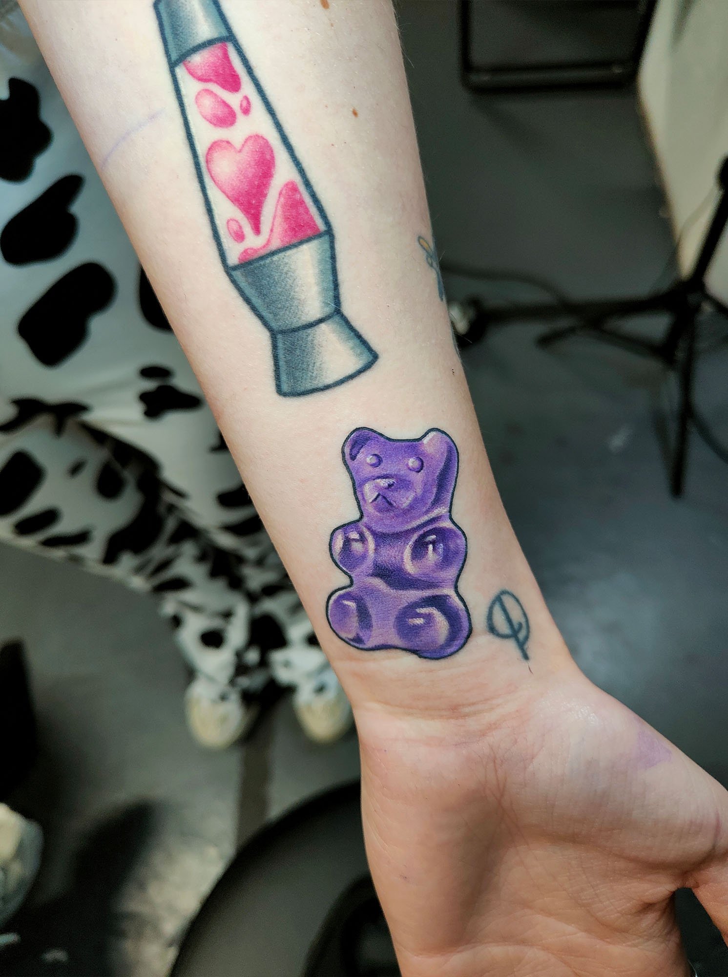 Tattoo of a purple gummy bear and a lava lamp on a forearm.