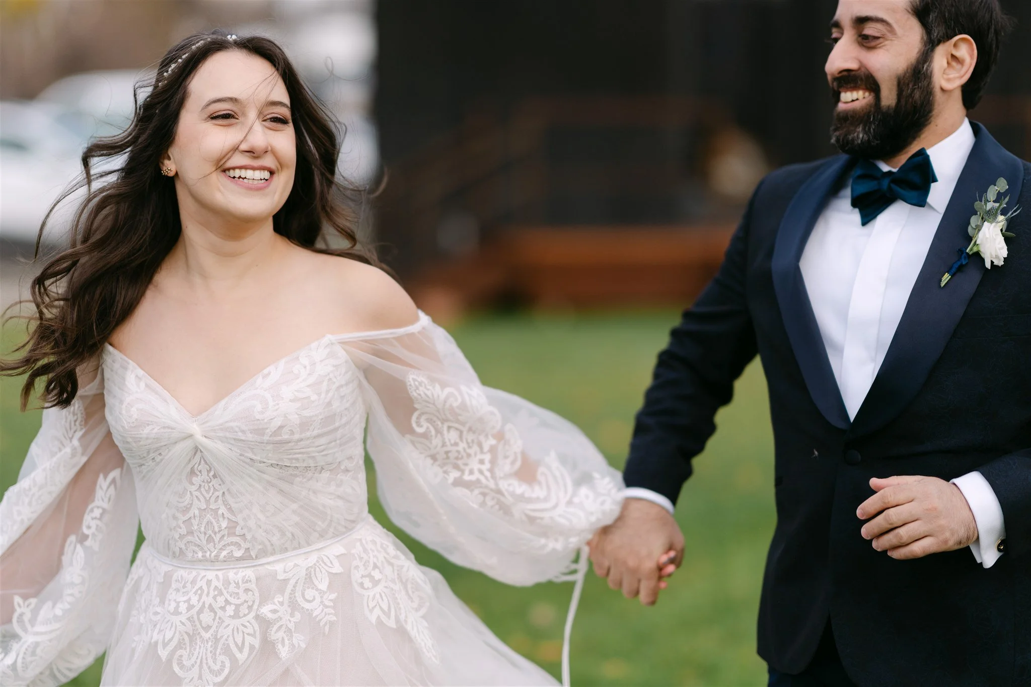 A bride and groom holding hands and smiling outdoors on a wedding day.