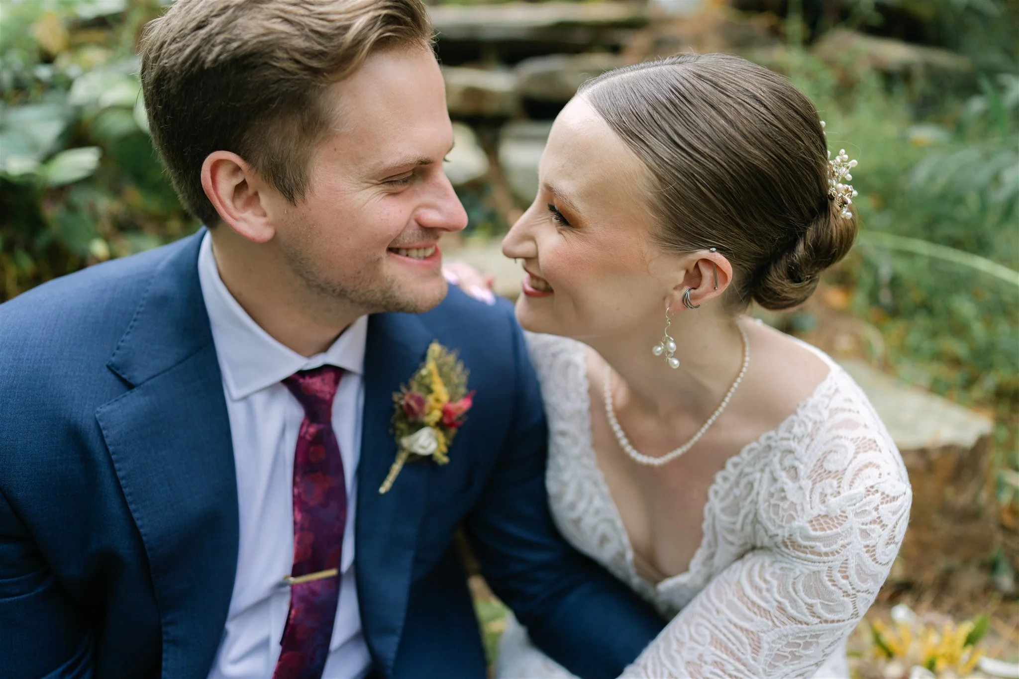 A bride and groom smiling and leaning close to each other outdoors.