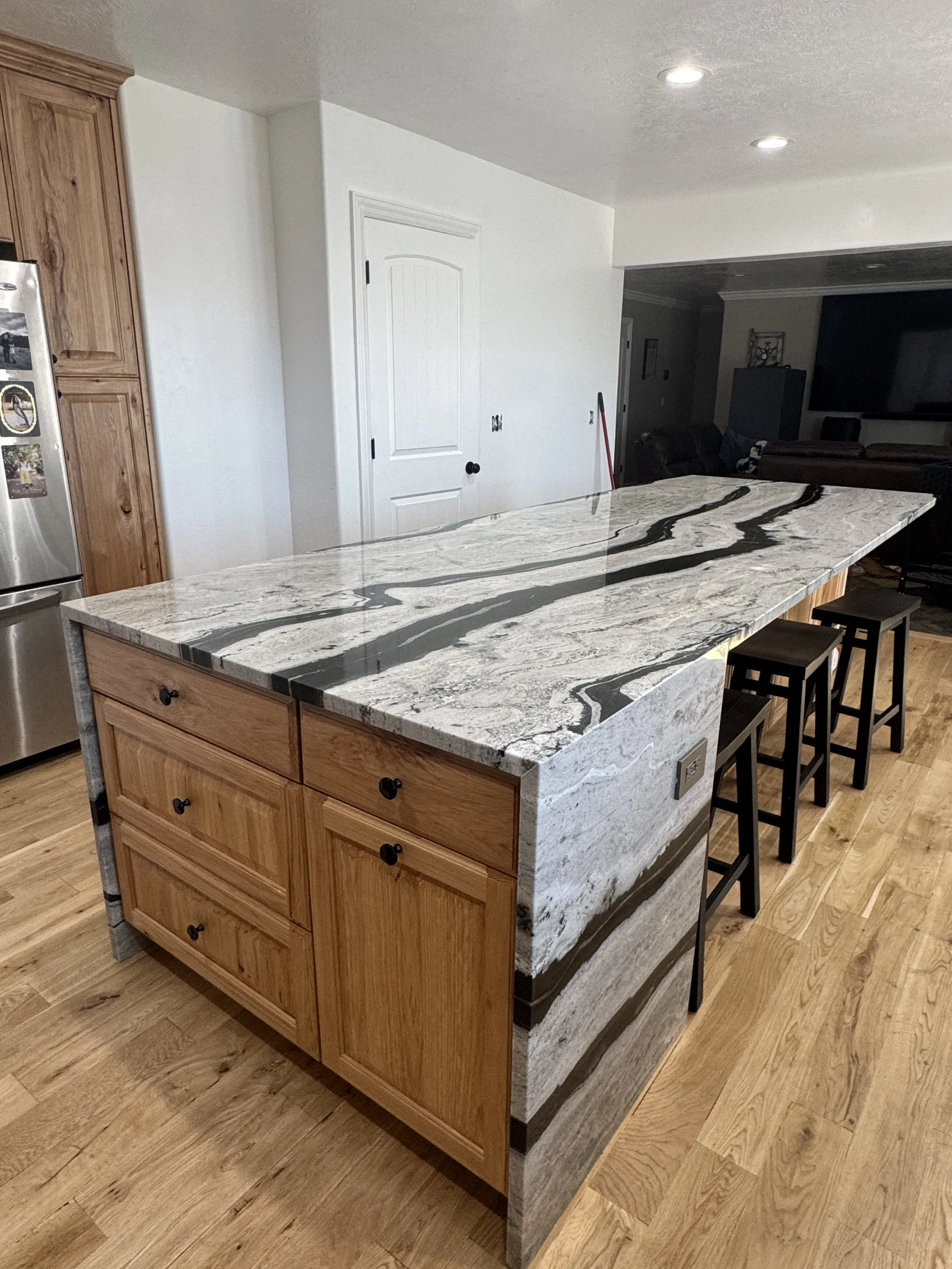 A kitchen island with a marble countertop and wood cabinets underneath, situated in a home with hardwood flooring and white walls.