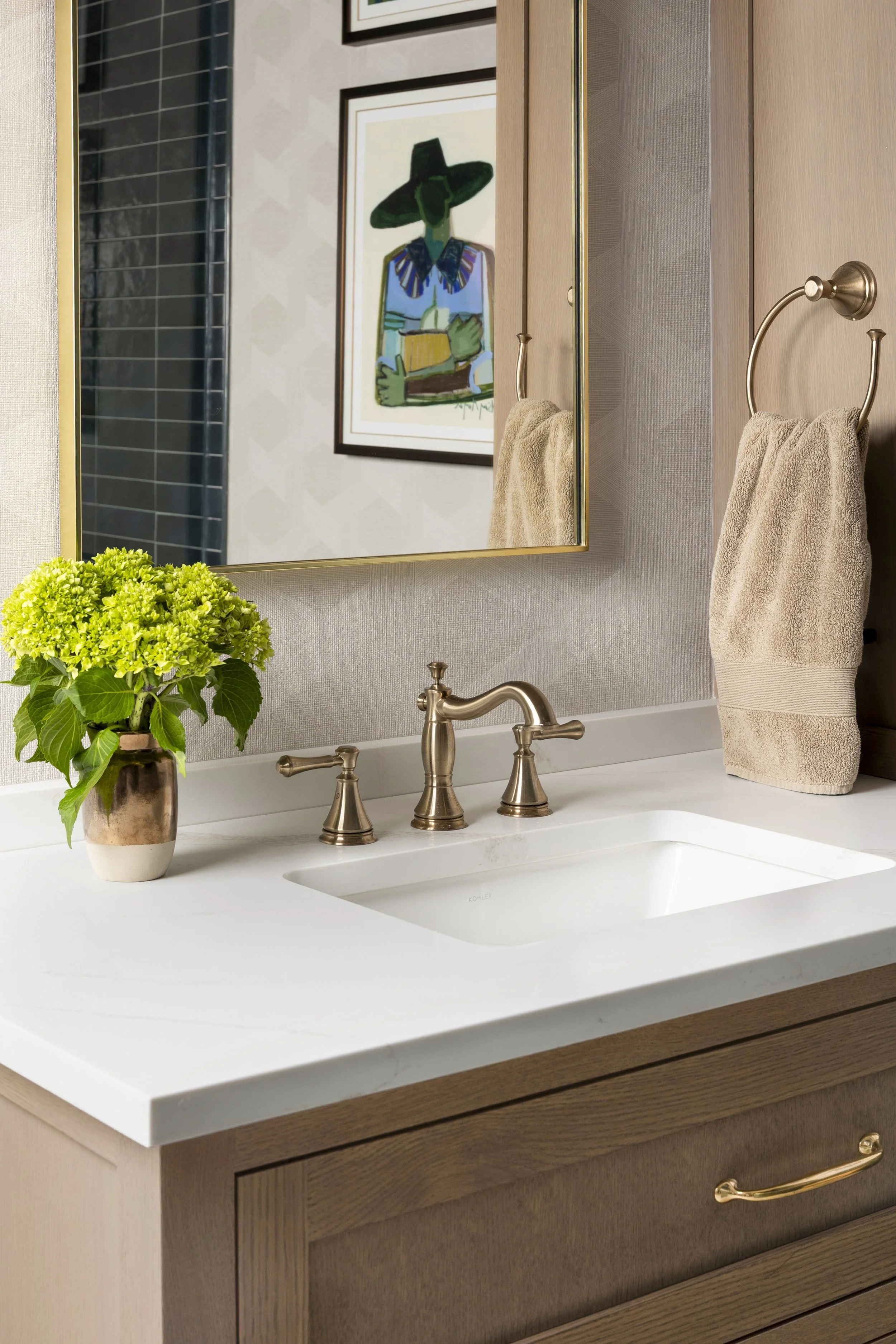 Close-up of a custom white oak bathroom vanity featuring a quartz countertop, brass faucet, designer mirror, and layered styling in a transitional Dallas-Fort Worth primary bathroom.