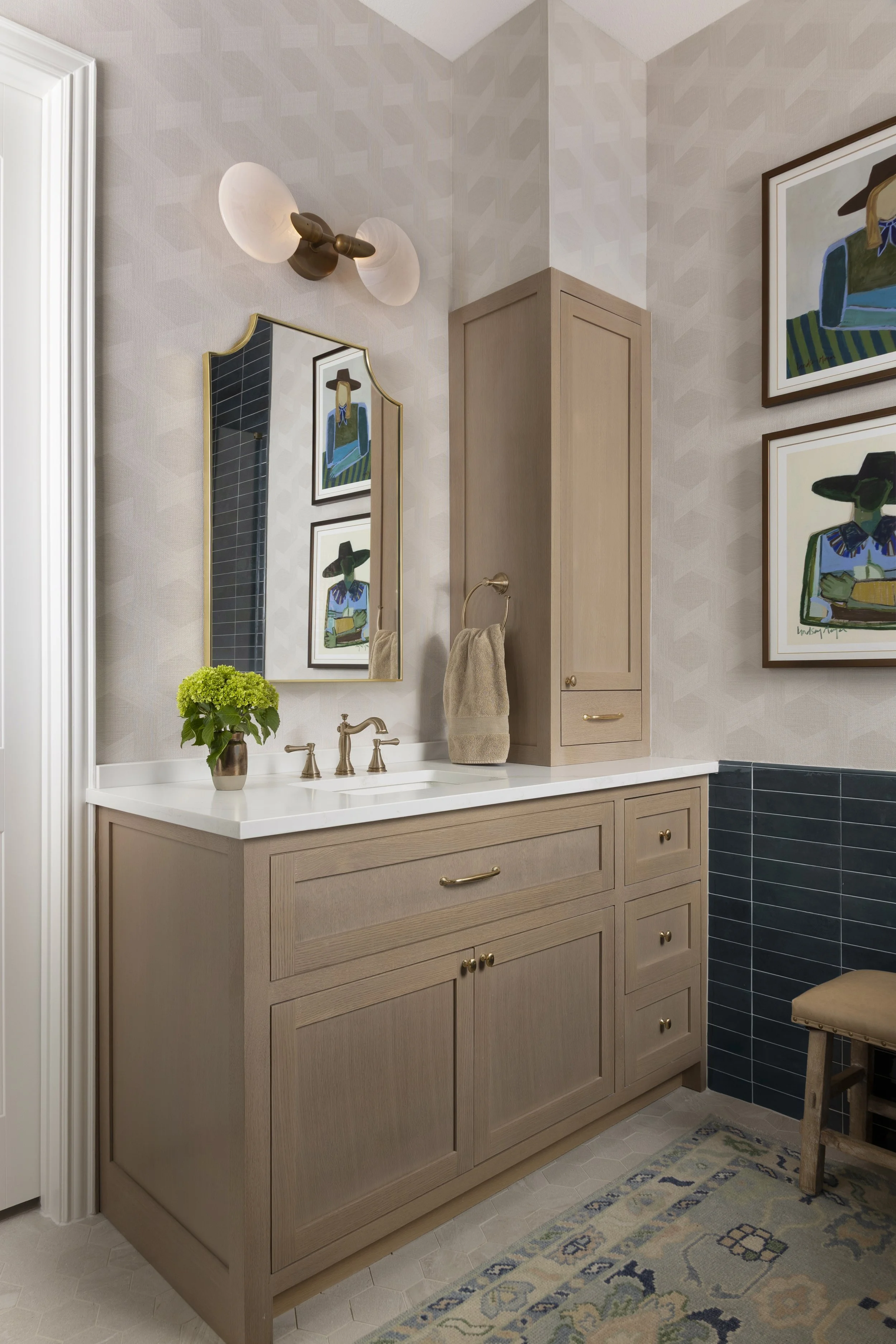 Custom white oak vanity with integrated makeup station, designer wallpaper, brass lighting, and layered textures in a transitional primary bathroom designed in the Dallas-Fort Worth area.