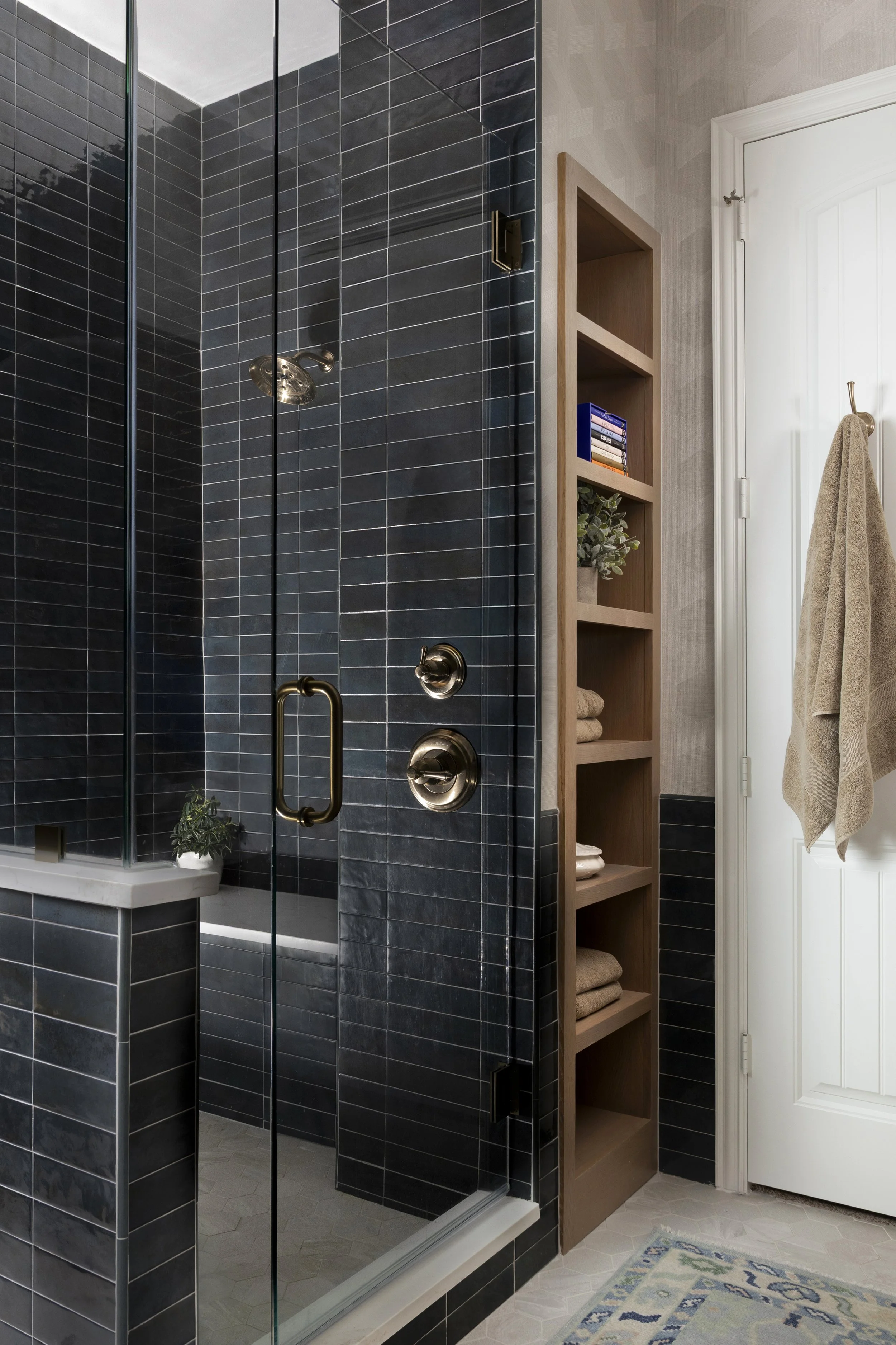 Walk-in primary bathroom shower with dramatic blue tile, frameless glass enclosure, custom white oak storage shelving, and warm brass fixtures in a Dallas-Fort Worth home.