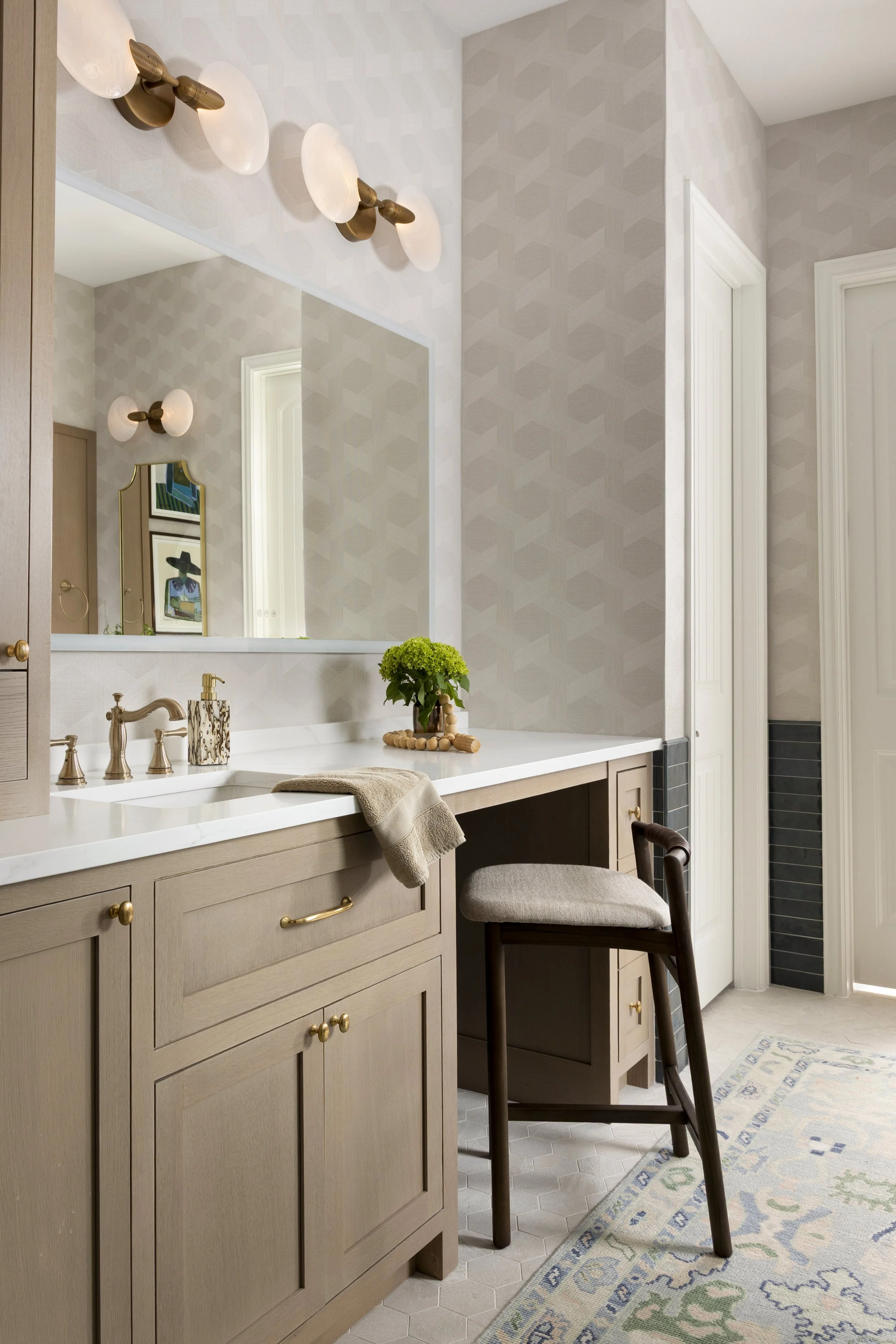 Transitional primary bathroom featuring a custom white oak vanity, quartz countertop, integrated storage tower, brass fixtures, designer wallpaper, and custom artwork in a Dallas-Fort Worth home.