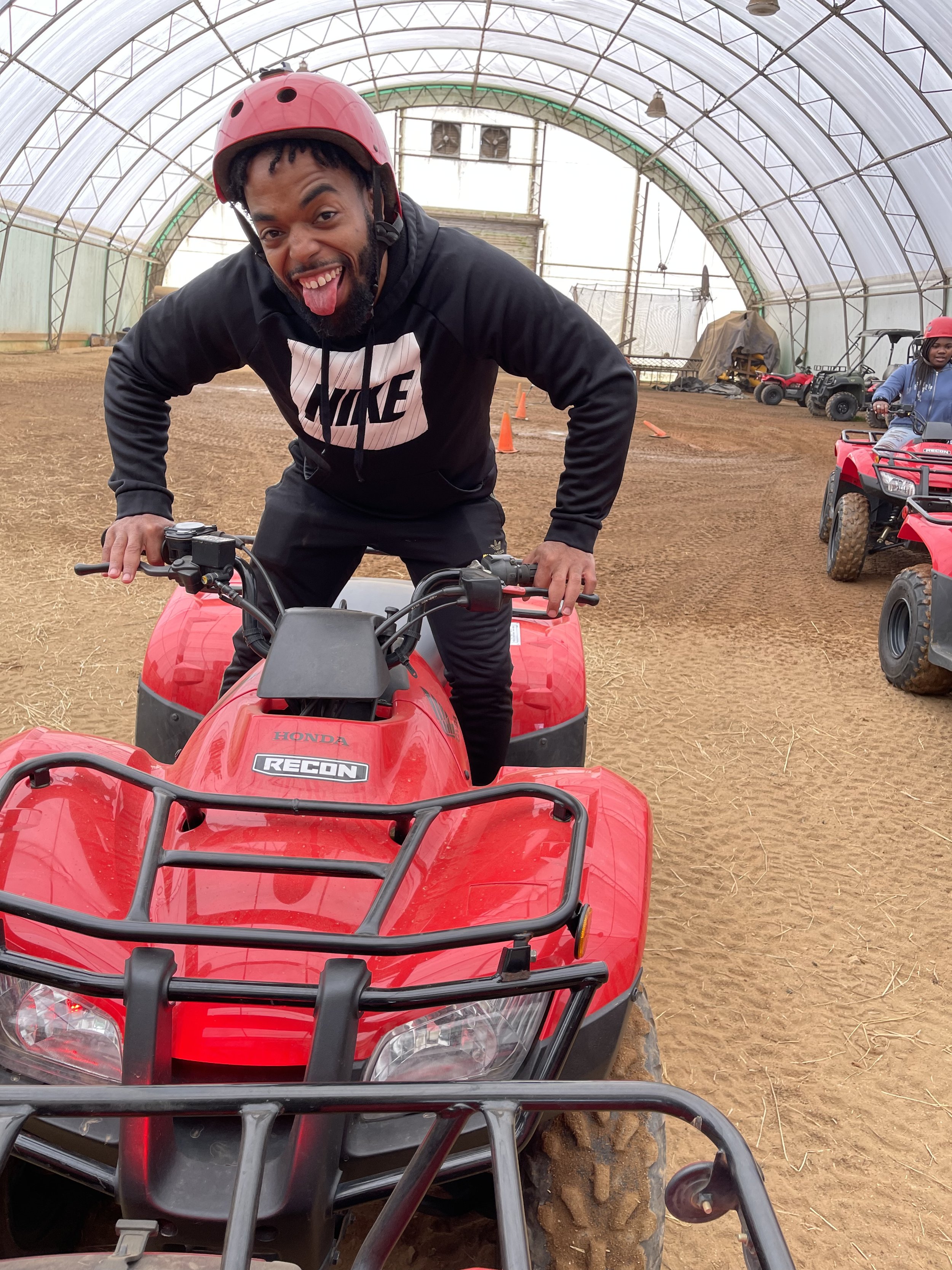 Person on a red Honda Recon ATV with a helmet, indoor dirt track setup.