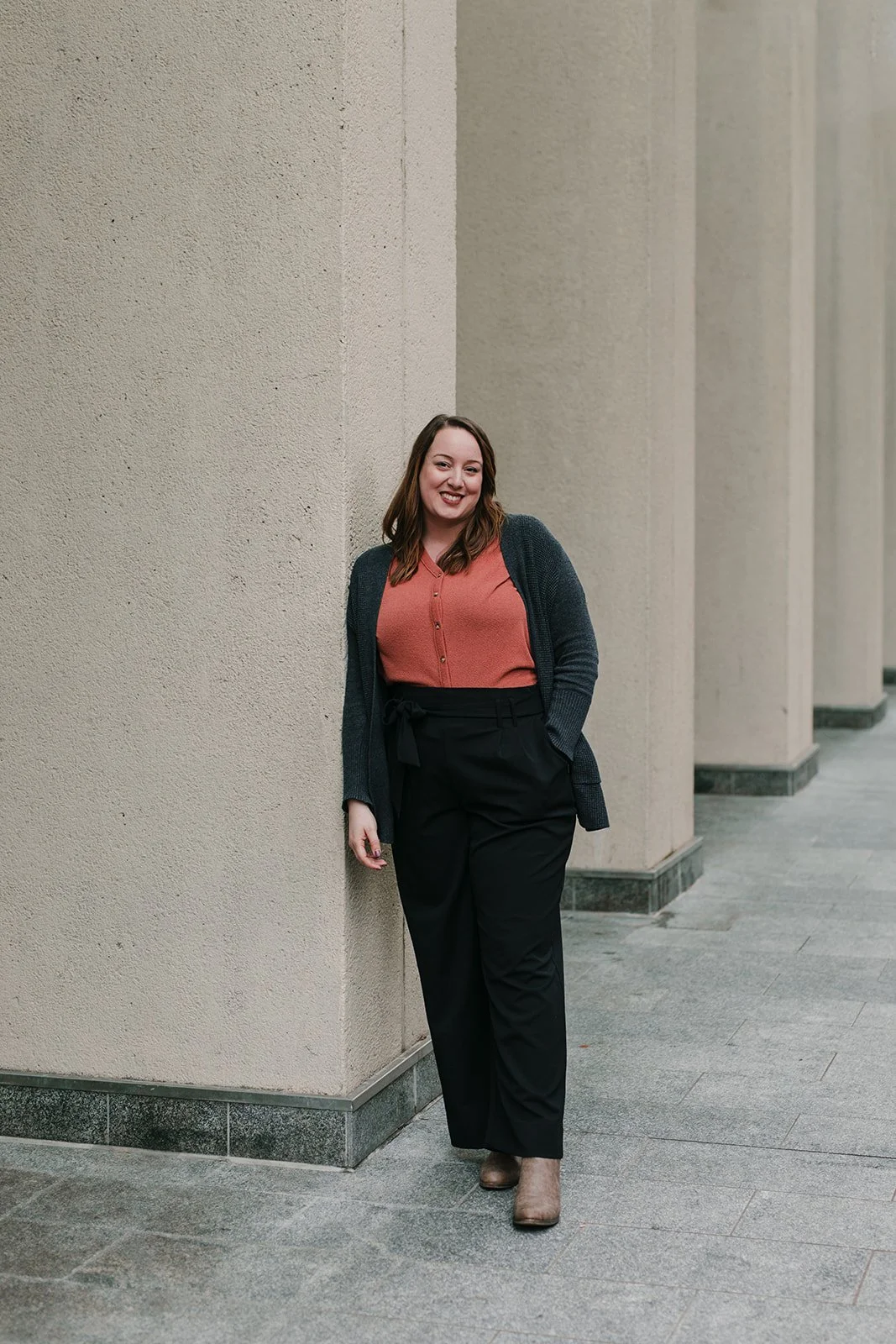Smiling woman with long, brown hair, stands next to a building.