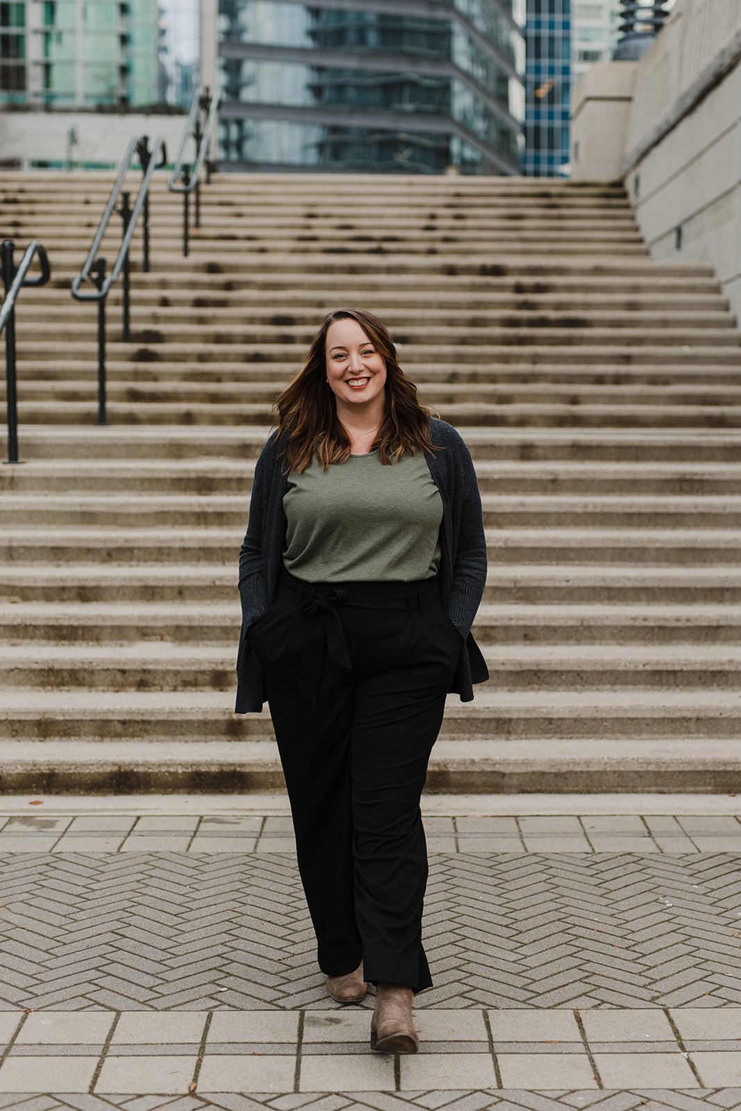 Smiling woman with long, brown hair walks in front of concrete steps.