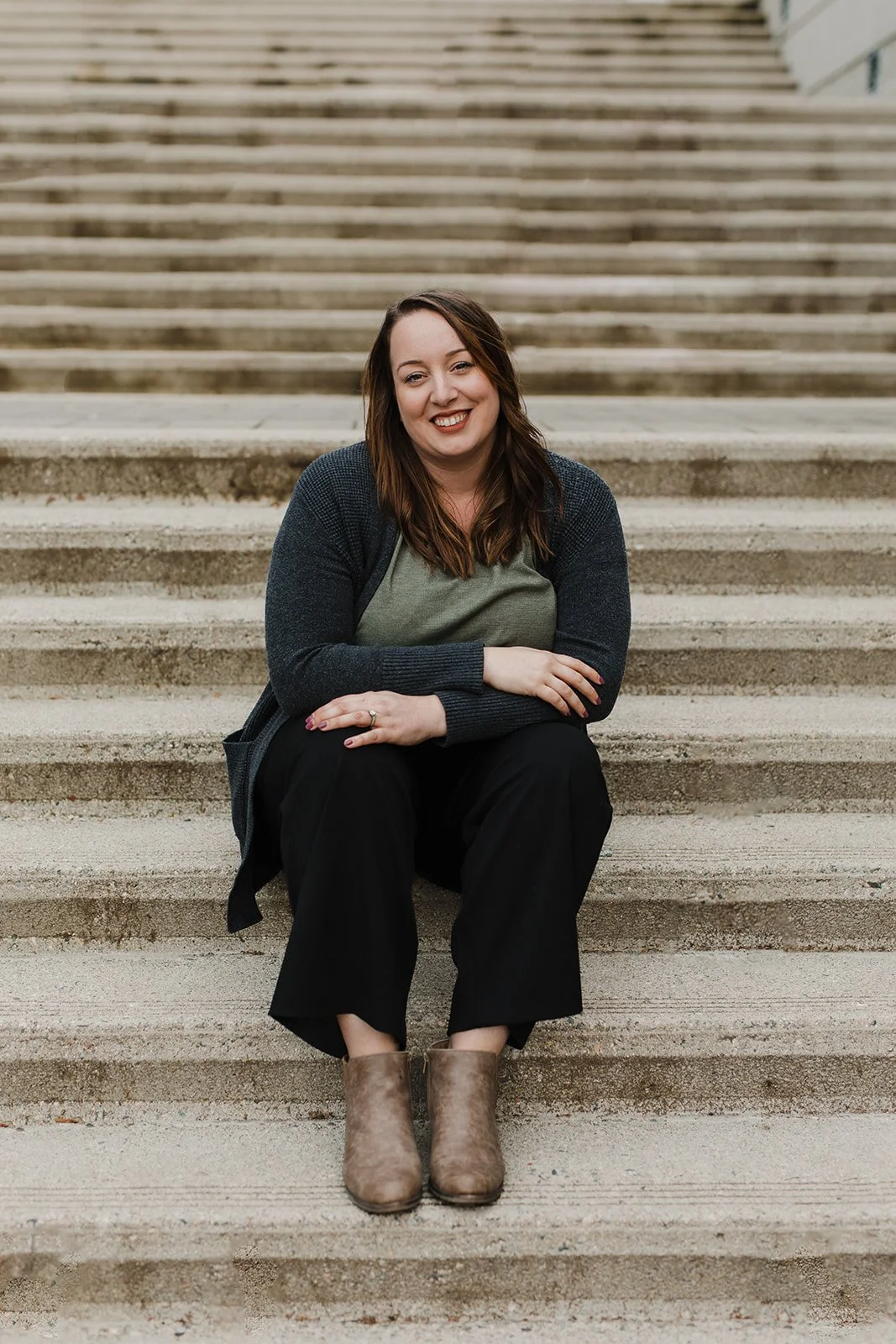 Smiling woman with long, brown hair sits on concrete steps.