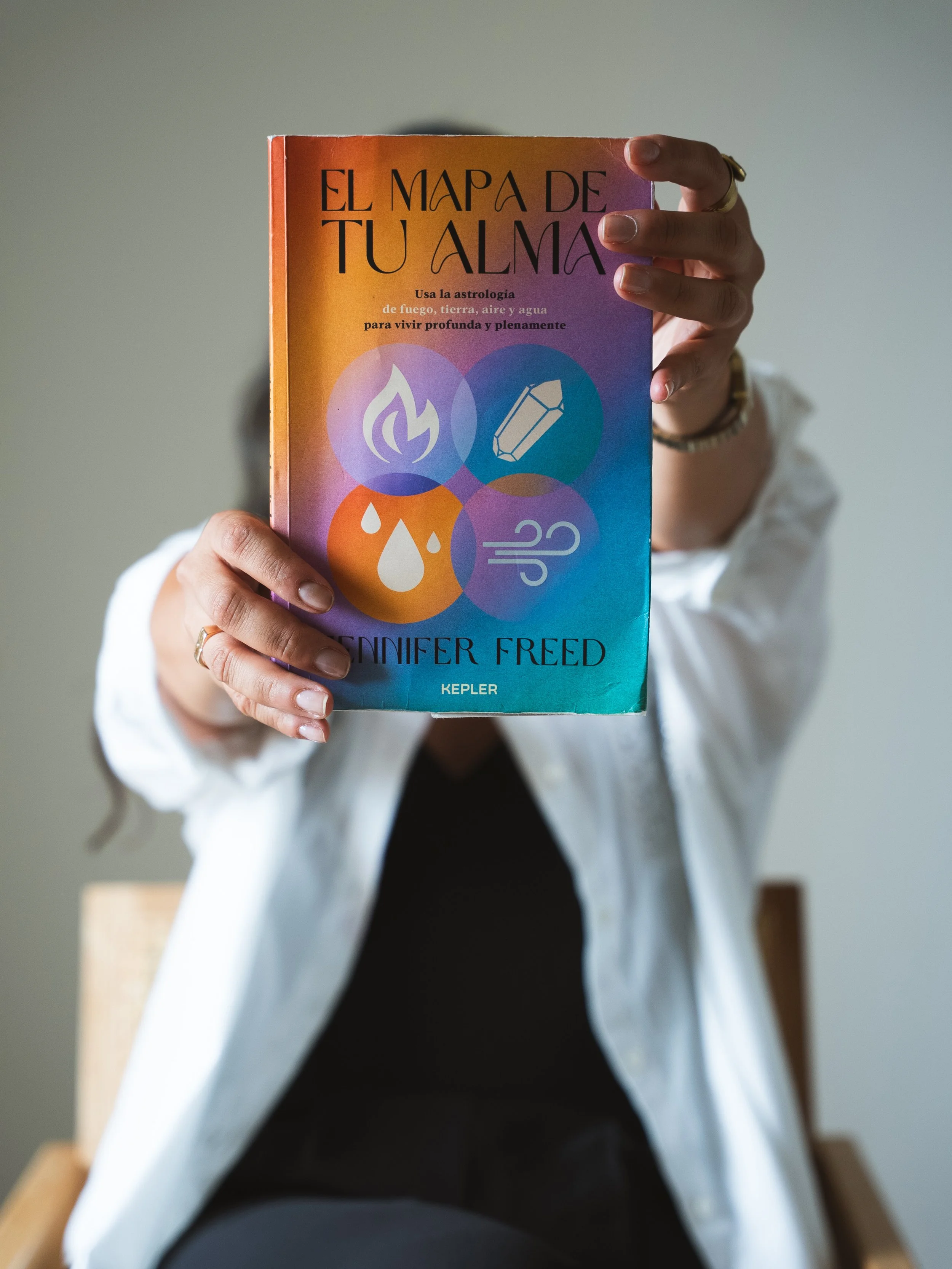 Persona sosteniendo un libro titulado 'El mapa de tu alma' con iconos de fuego, agua, aire y tierra en la portada.