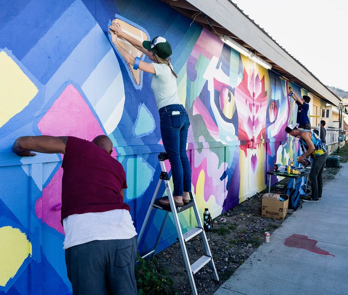Artists painting a colorful mural on a building wall, featuring abstract geometric patterns.