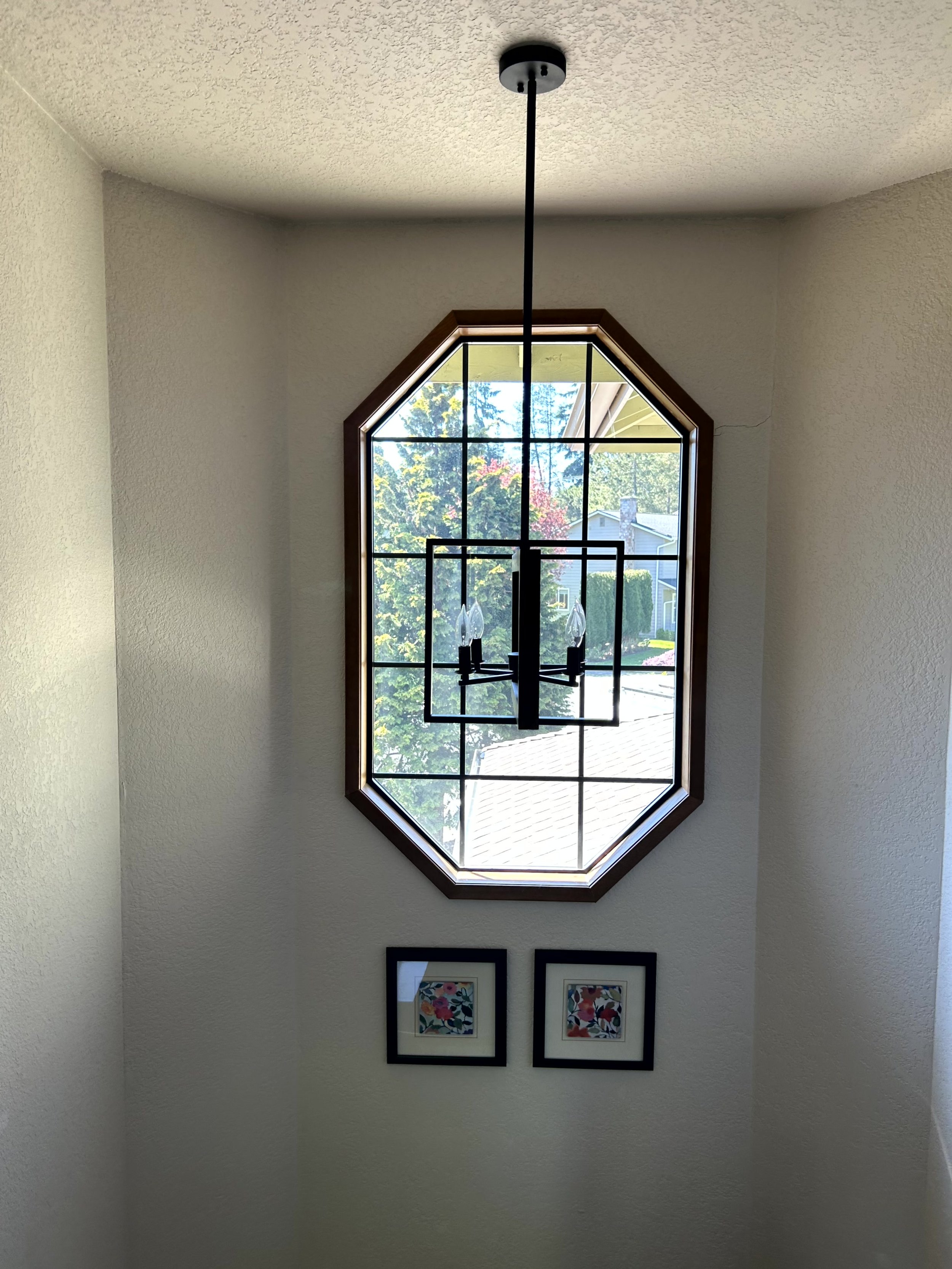 An interior wall with an octagonal window and a black frame chandelier hanging from the ceiling.