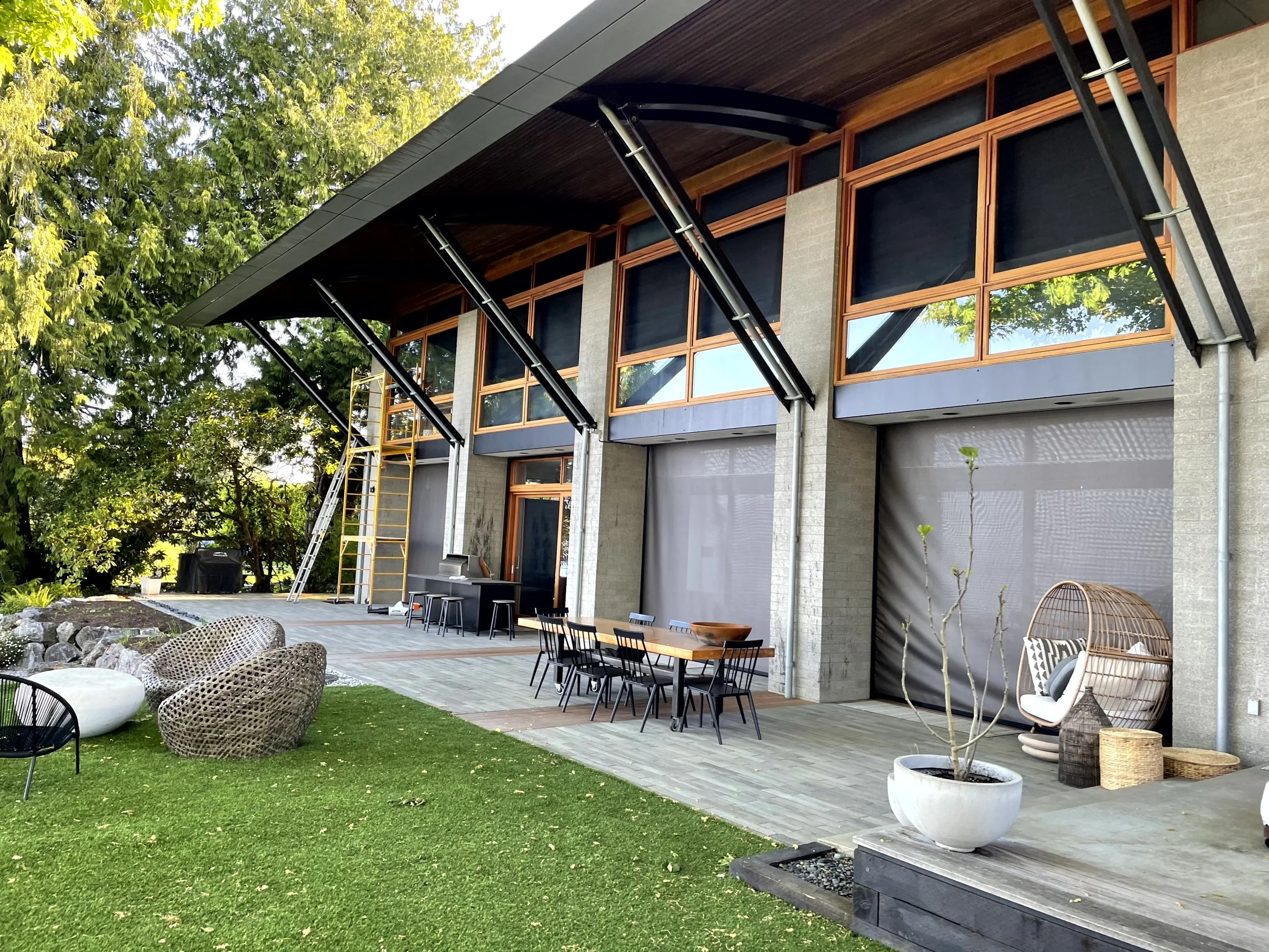 Modern house with outdoor patio, green lawn, patio furniture, potted plants, and large windows.