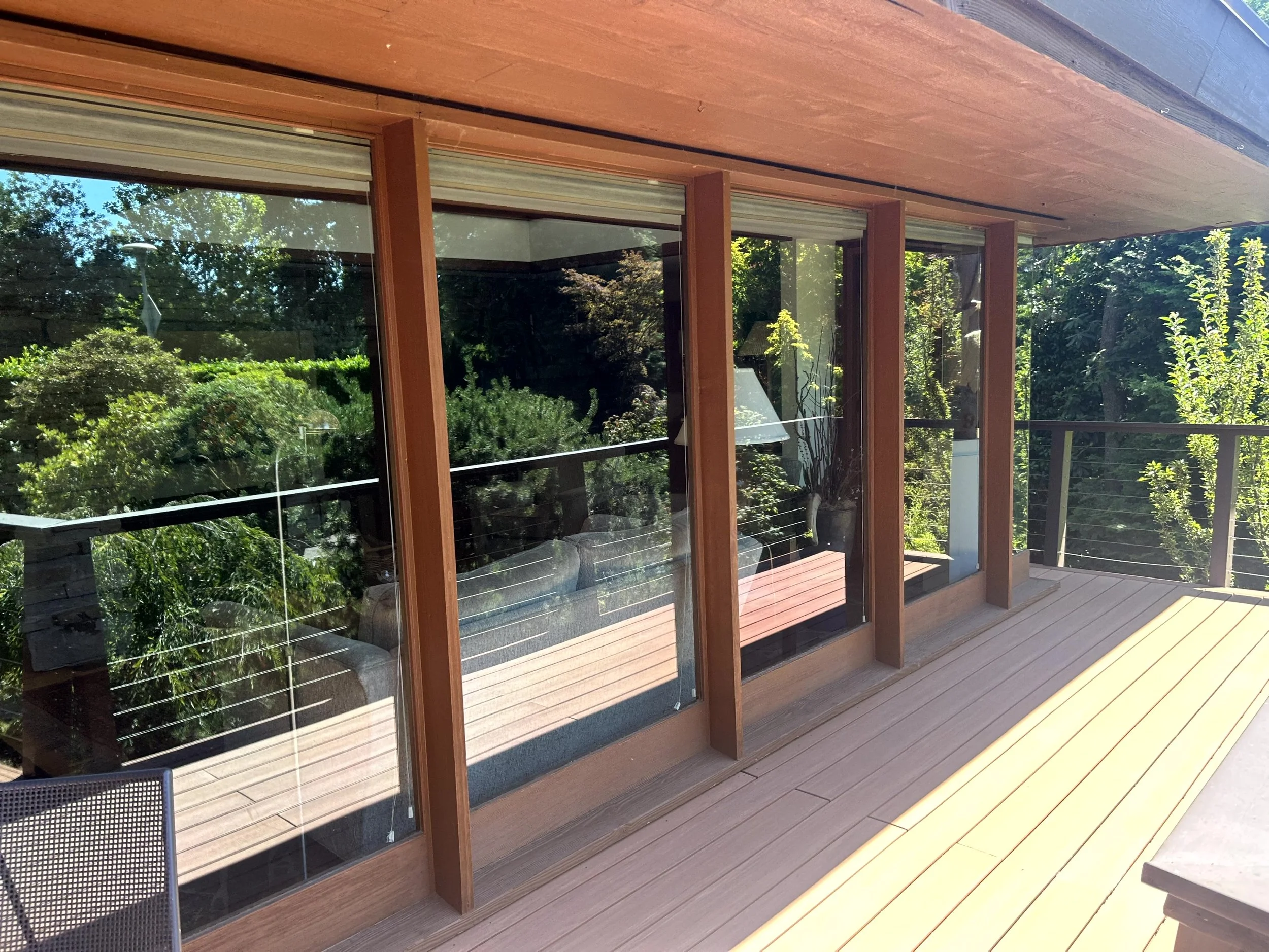 A wooden deck with large glass sliding doors and a view of greenery and trees outside.