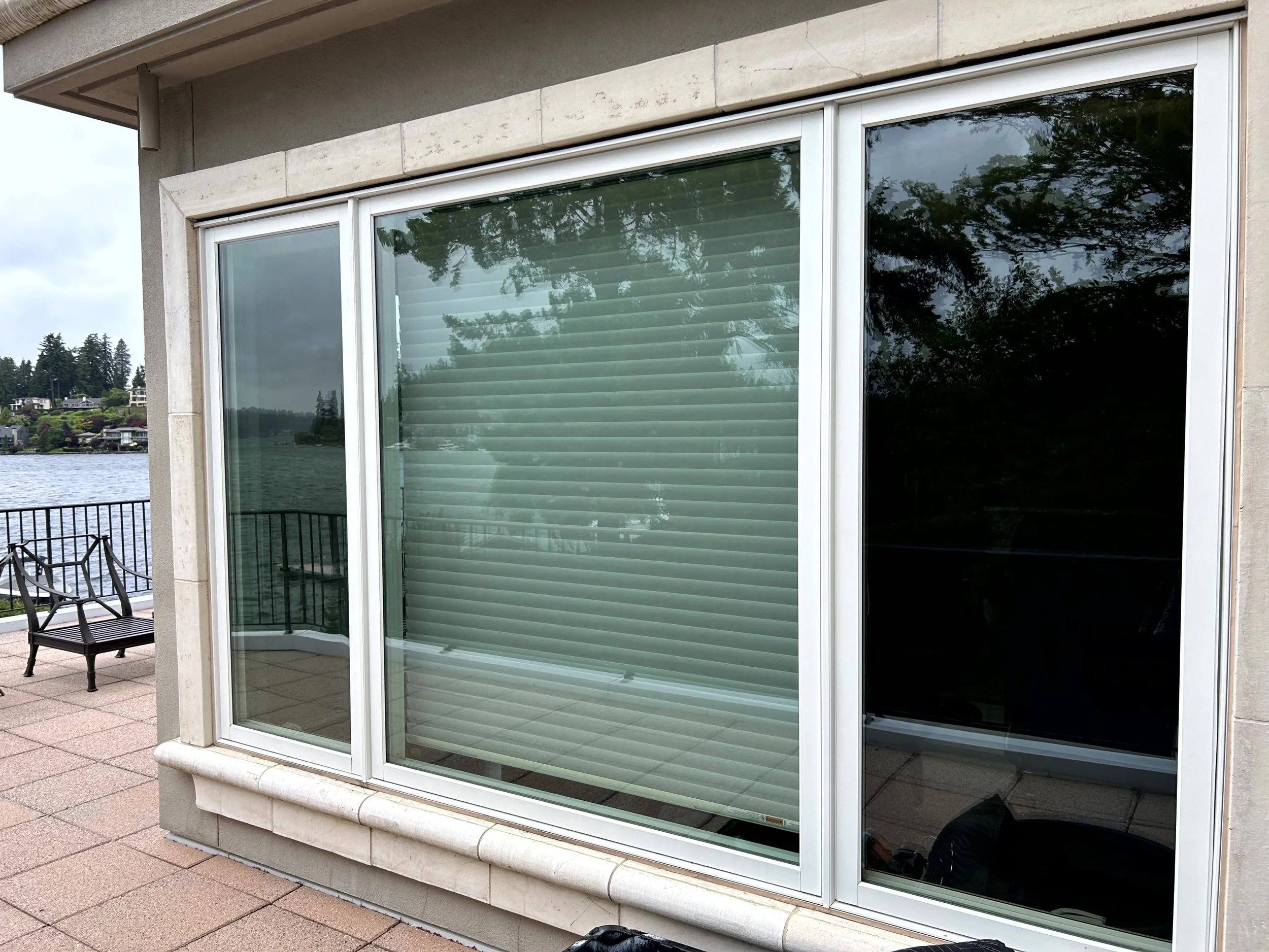 Glass sliding door with interior blinds, part of a building exterior, with a deck and a lakeside view in the background.