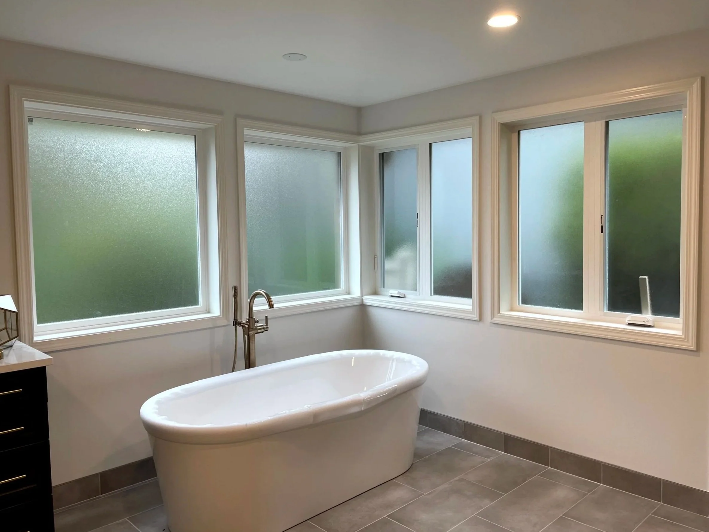 Modern bathroom with a white freestanding bathtub, multiple frosted windows, and gray tiled floor.
