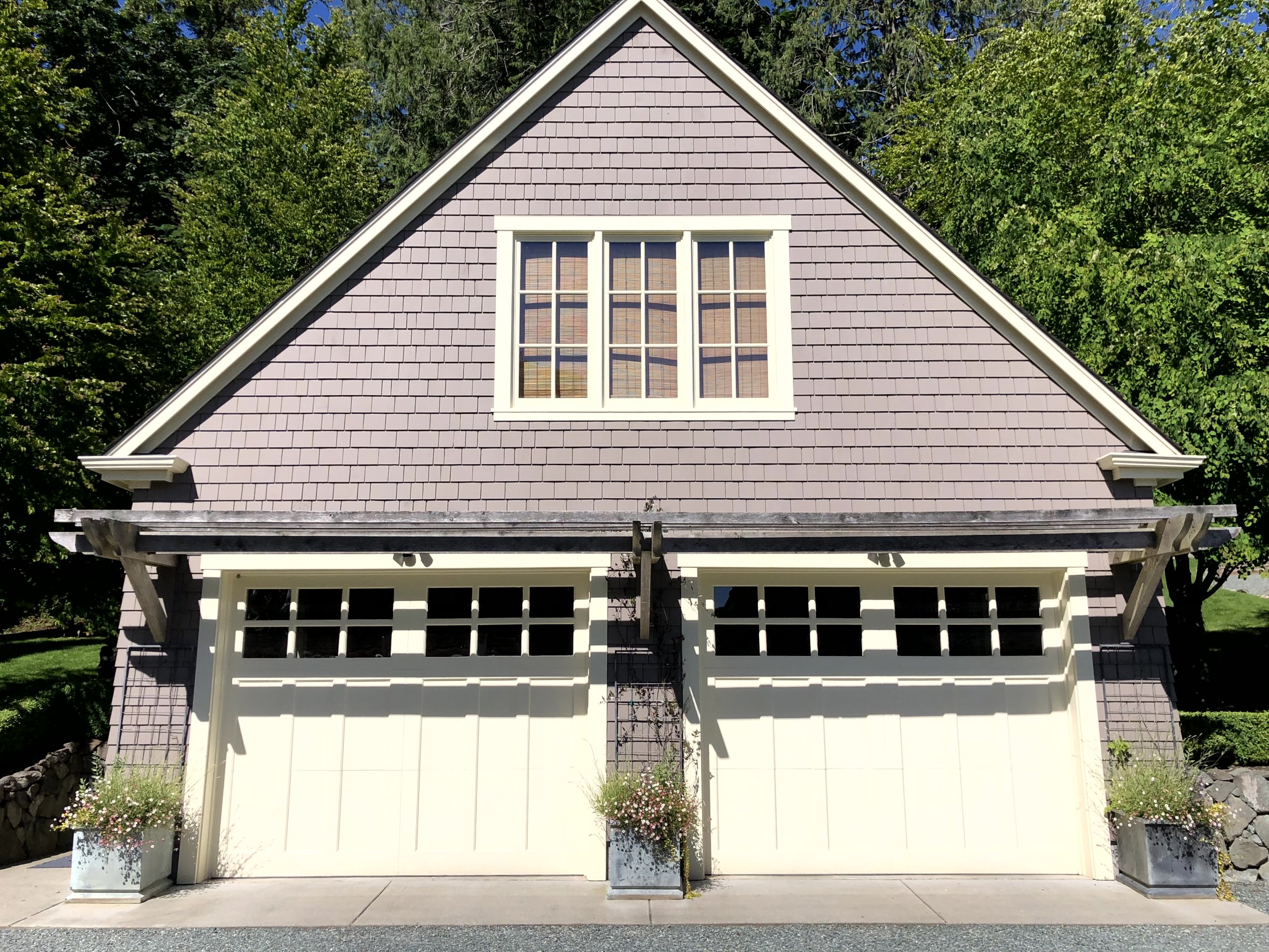 Front of a two-story house with a purple shingle exterior, white garage doors with windows, and a flower planter on each side of the garage.