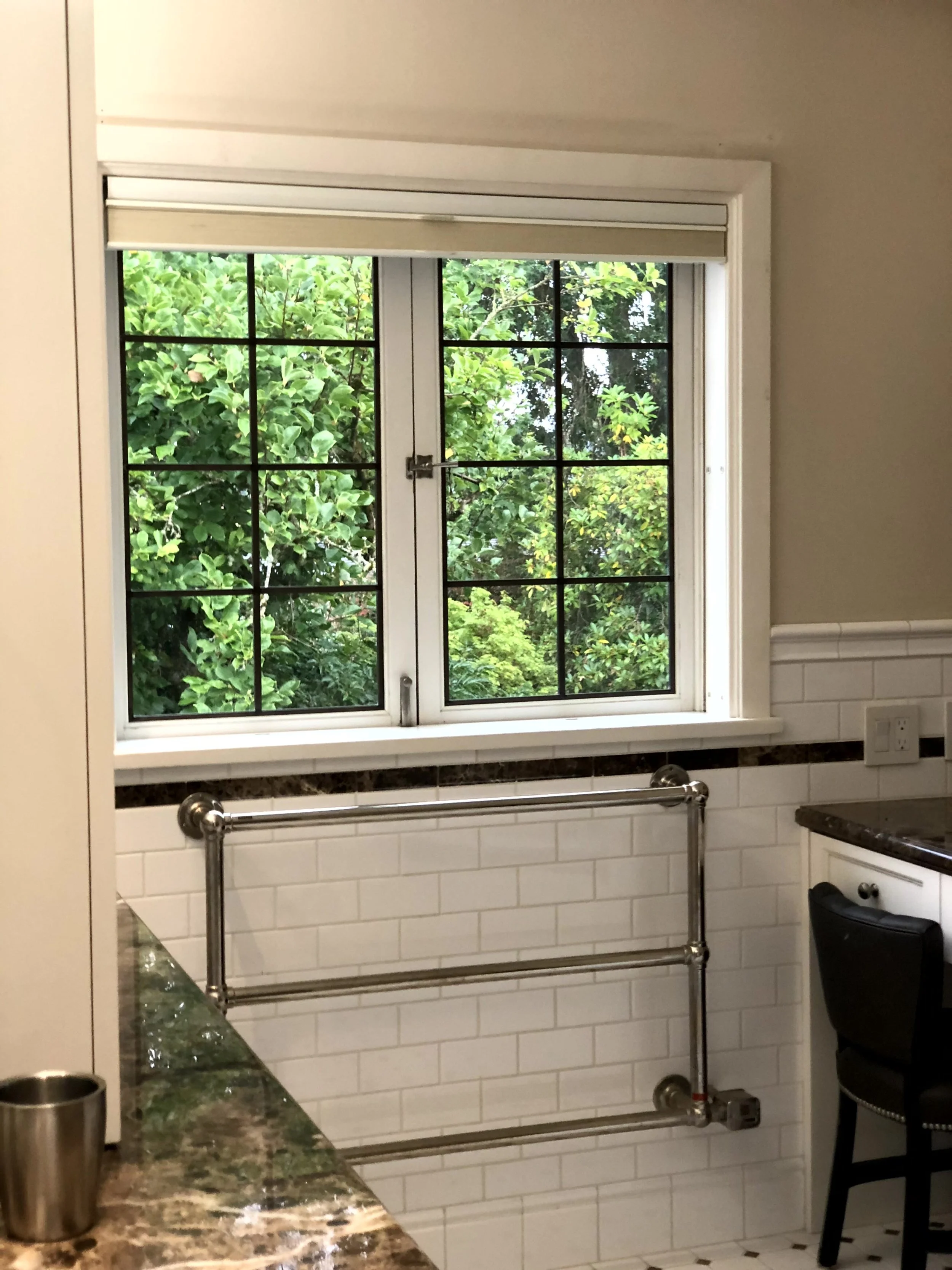 Kitchen window with black grid pattern overlooking green trees and plants outside.
