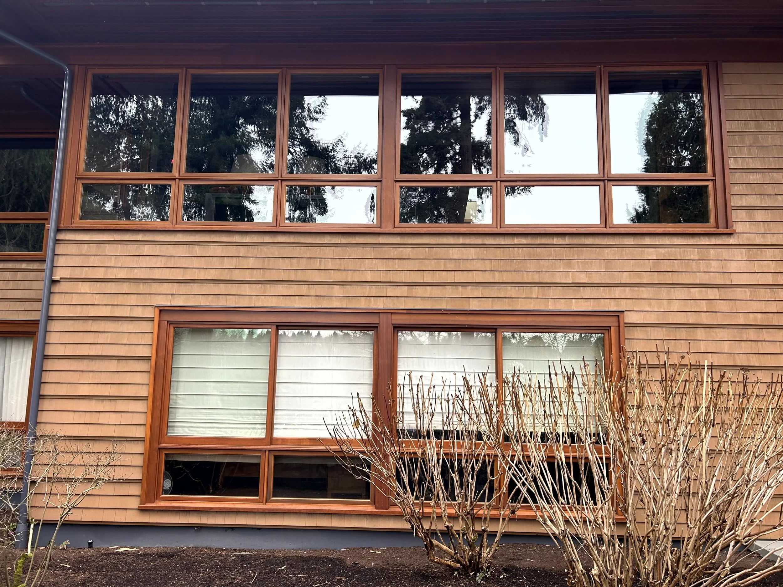 Front view of a multi-story house with large wooden-framed windows and a shrub in front