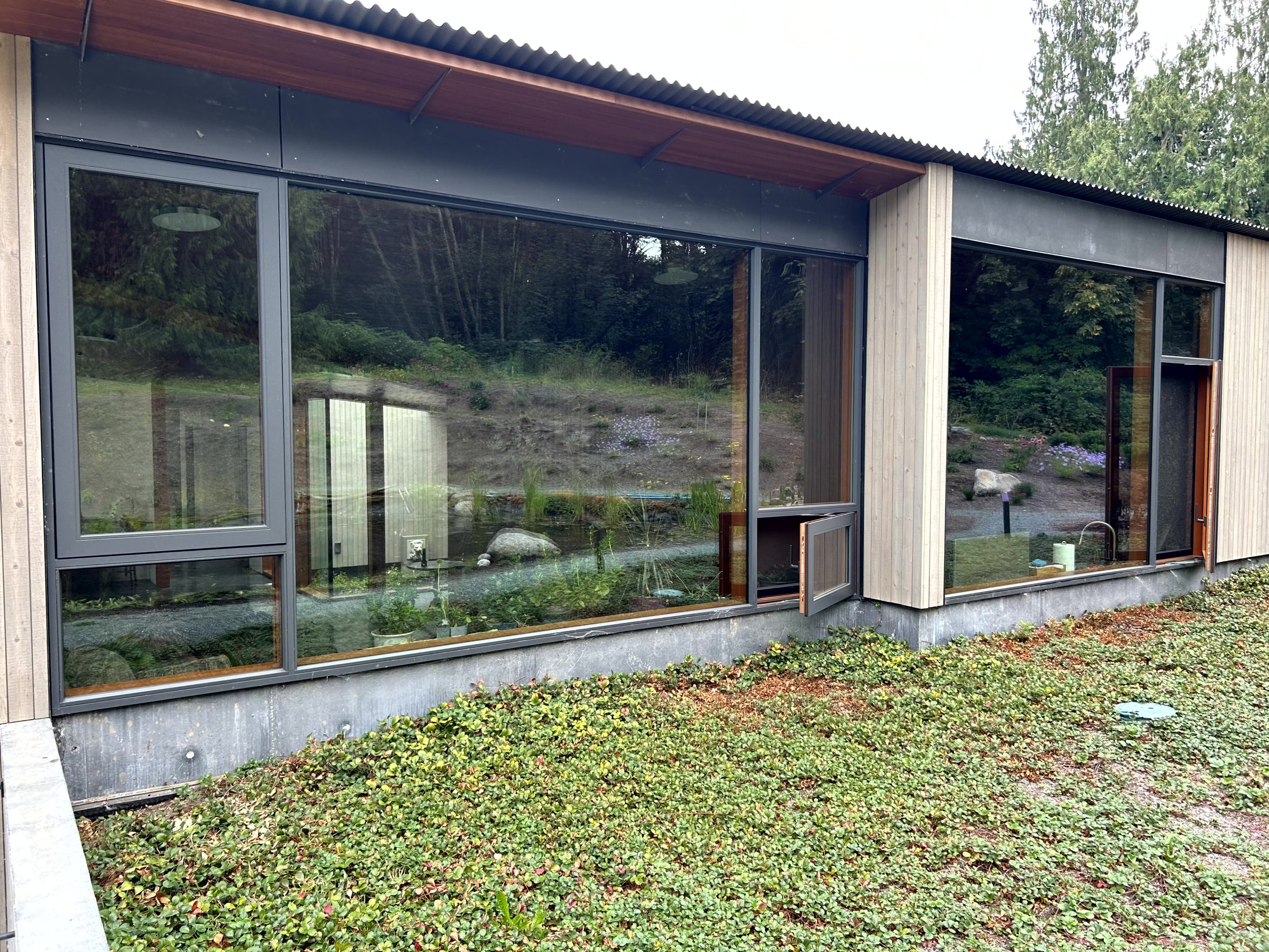 Modern building with large glass windows and wooden exterior, surrounded by greenery and a garden.