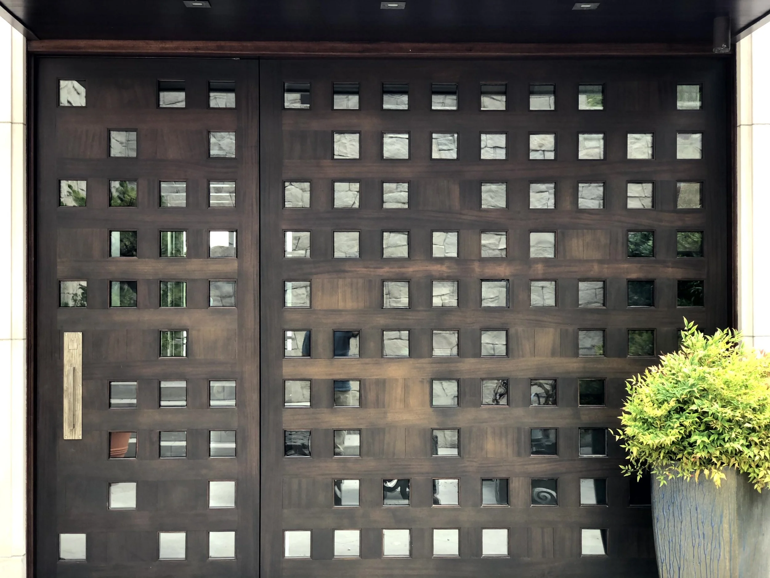 A large wooden garage door with square glass windows arranged in a grid pattern, and a small plant in a large blue pot on the right side.