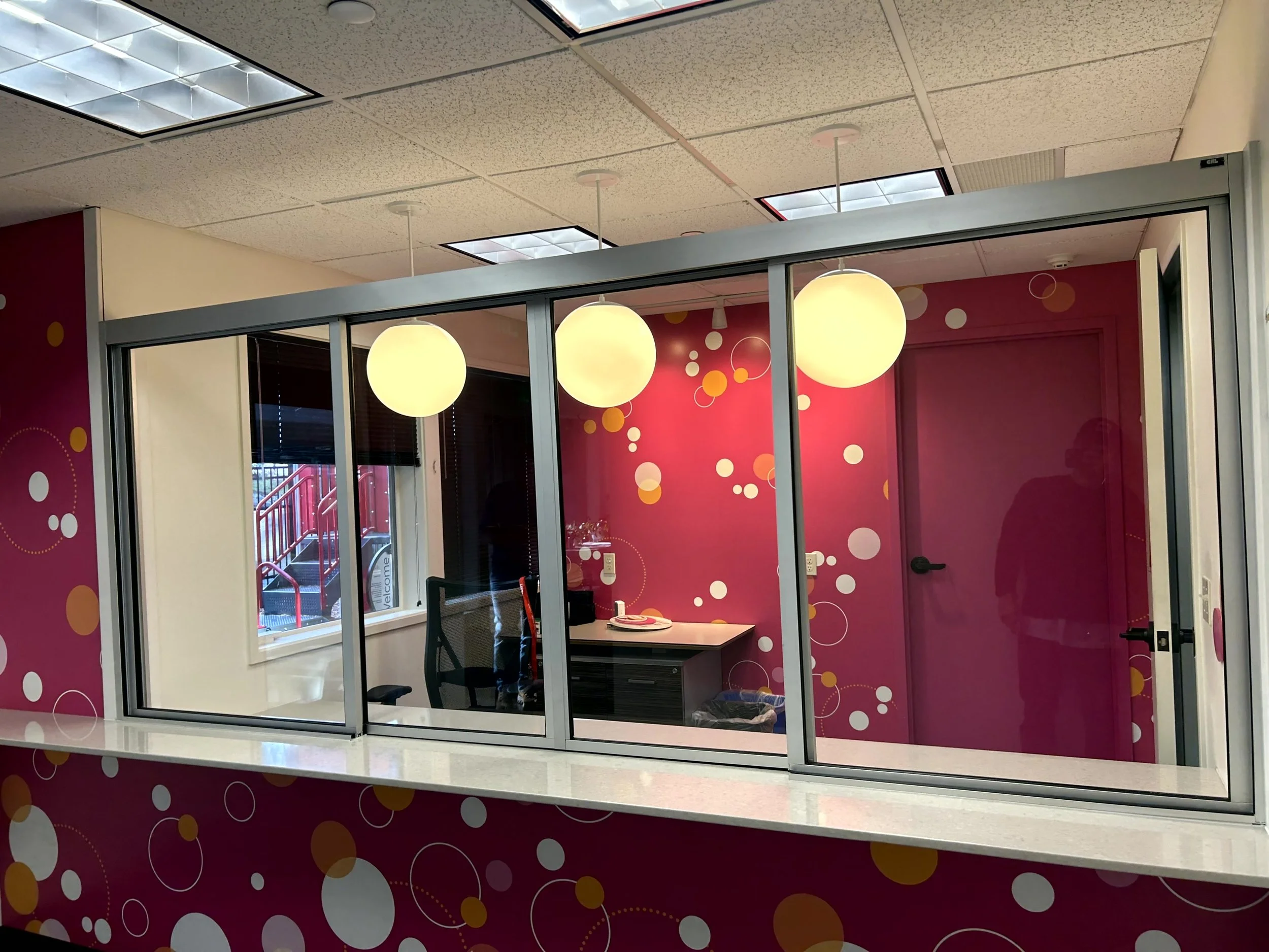 Office reception area with a pink and white polka dot theme, glass window, and hanging round light fixtures.