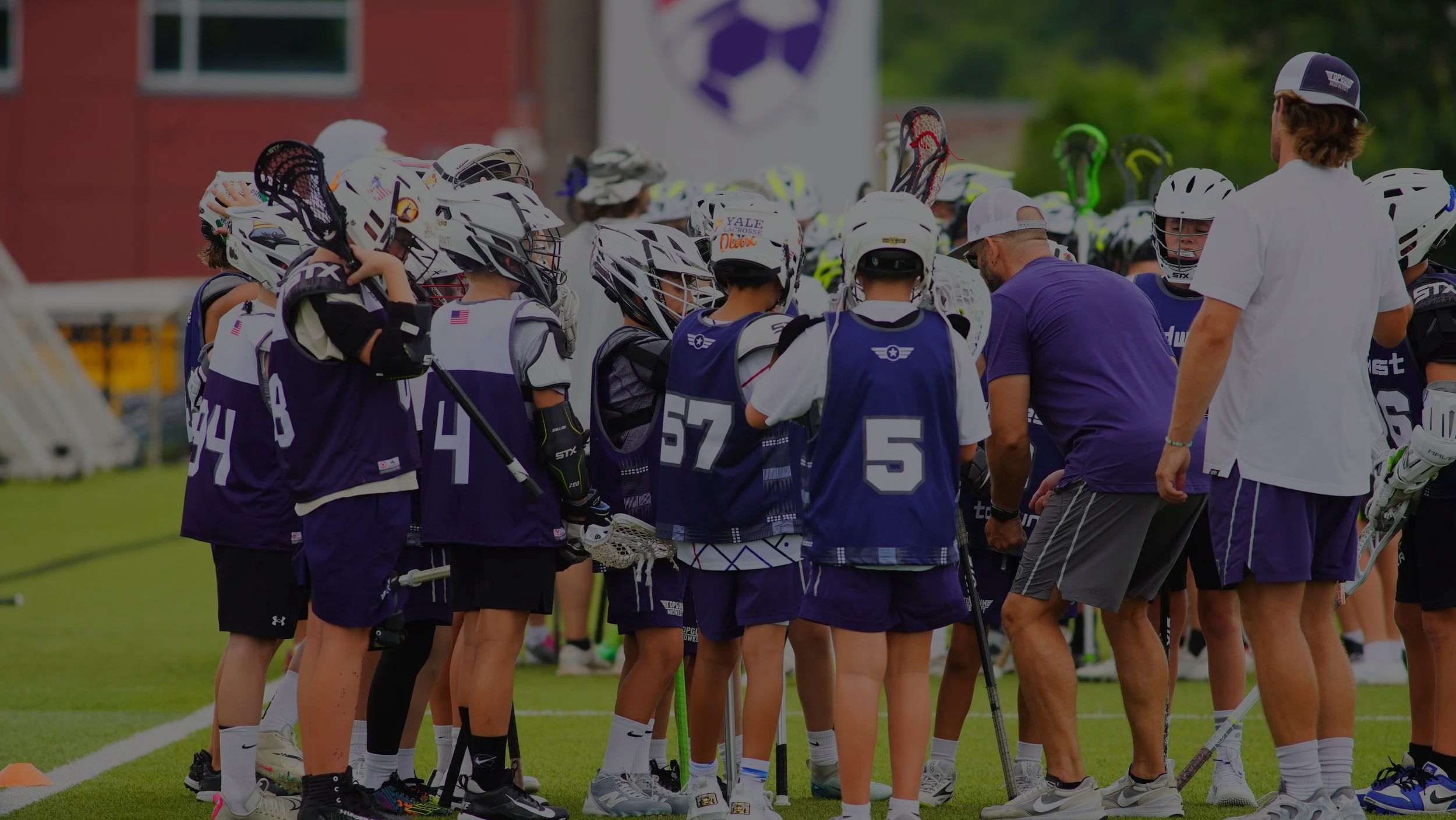 Lacrosse team huddled with coaches on a grassy field during practice.