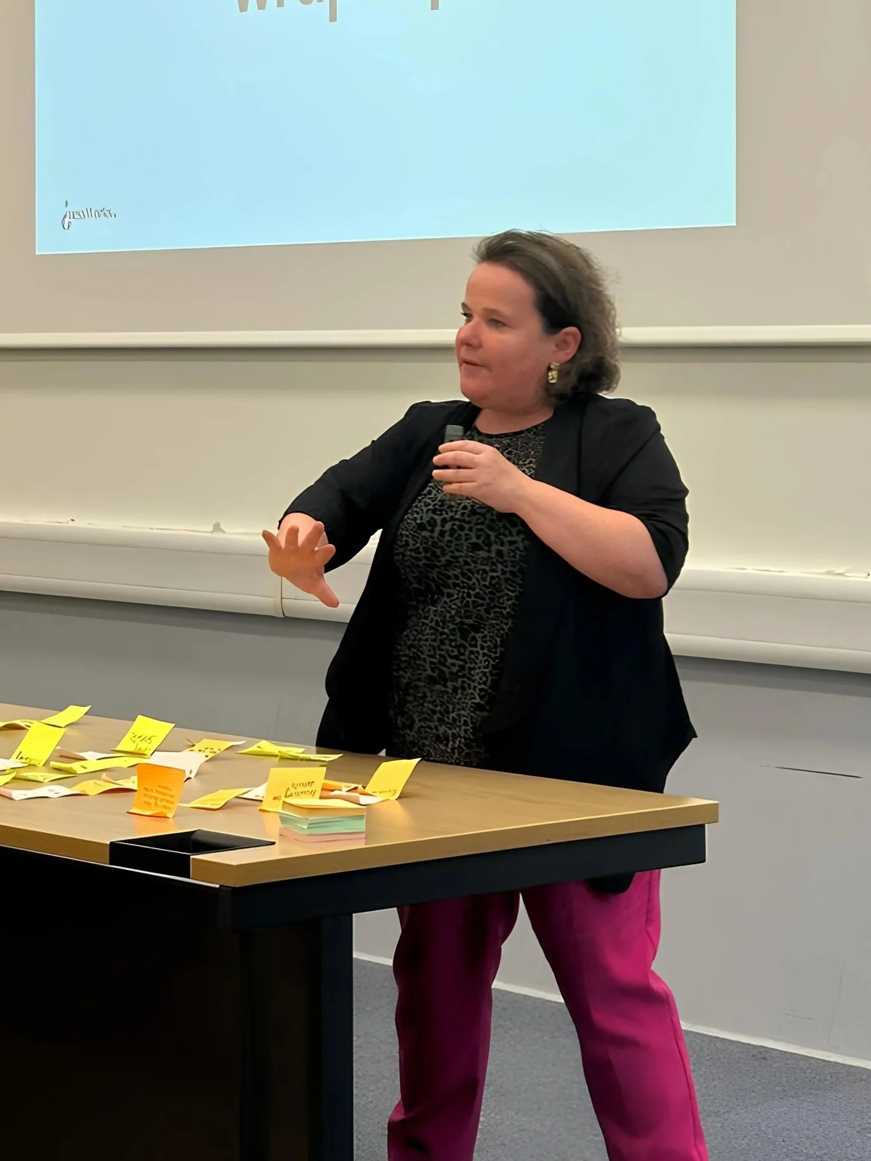 Sascha leading an interactive workshop, standing by a table covered in handwritten sticky notes while gesturing to an audience