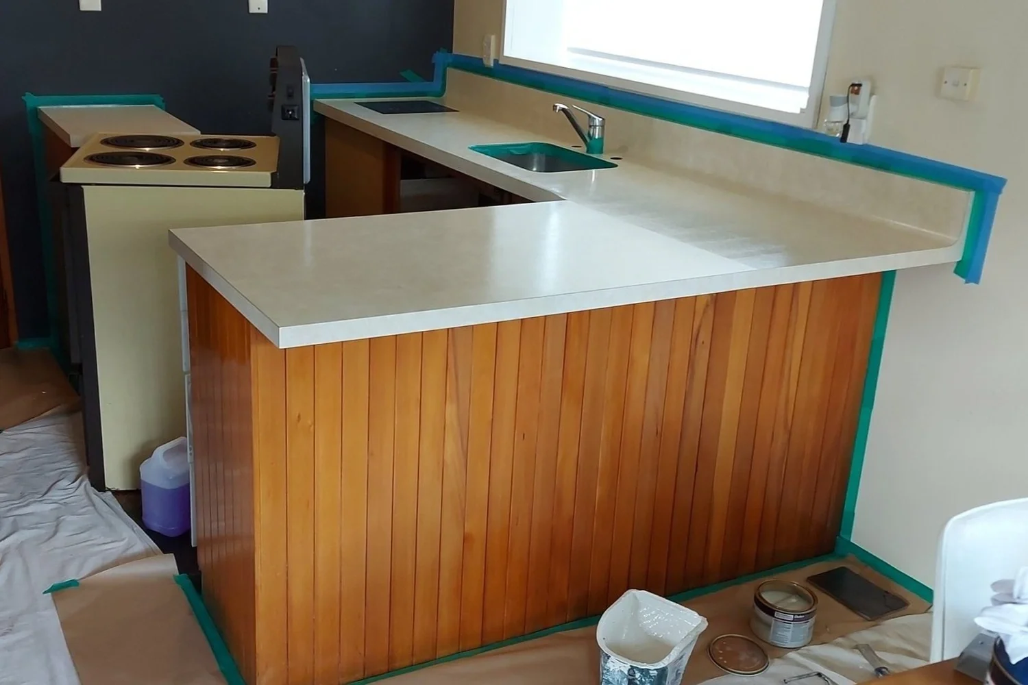 Kitchen repaint in progress in Christchurch, showing masking and preparation before revitalising timber cabinetry with a fresh white finish.