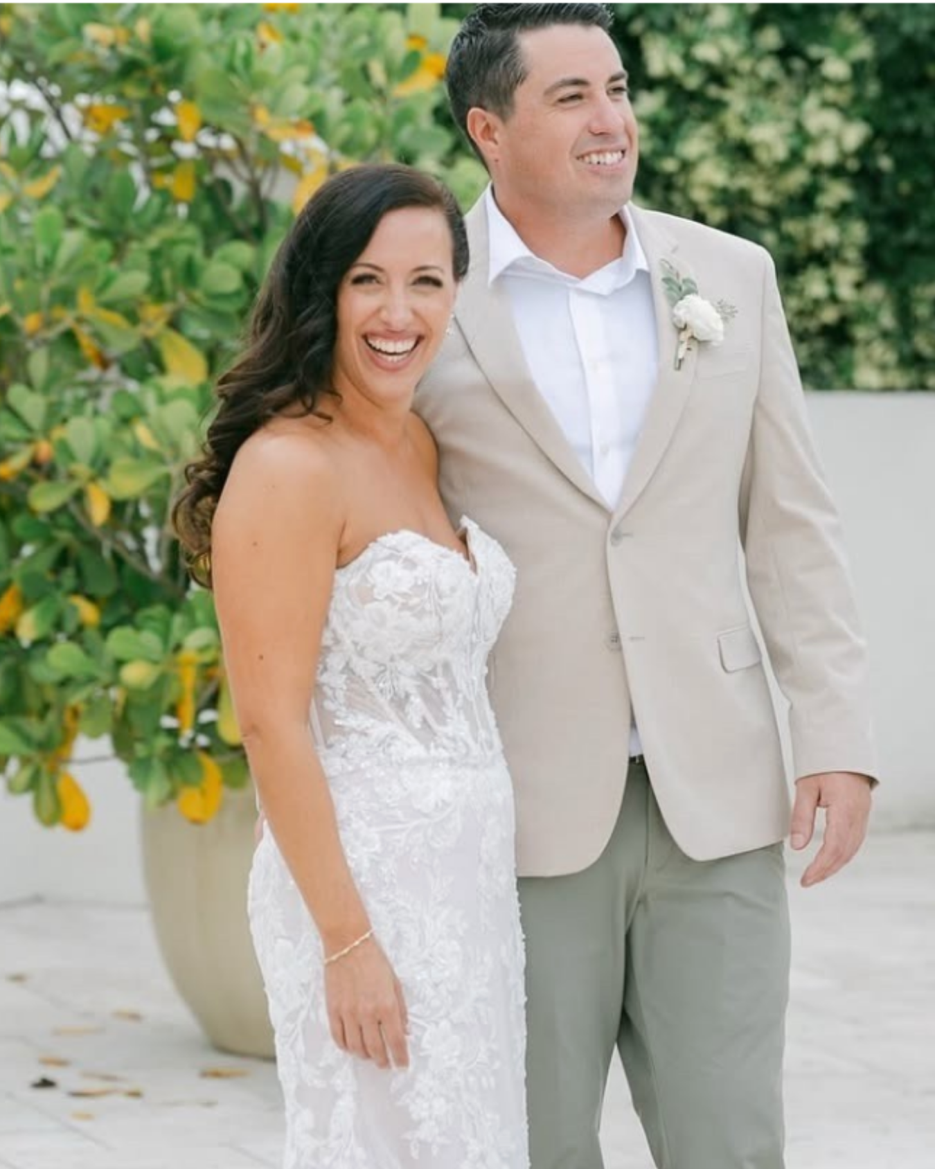 A bride and groom smiling at each other during their wedding, outdoors with greenery in the background.