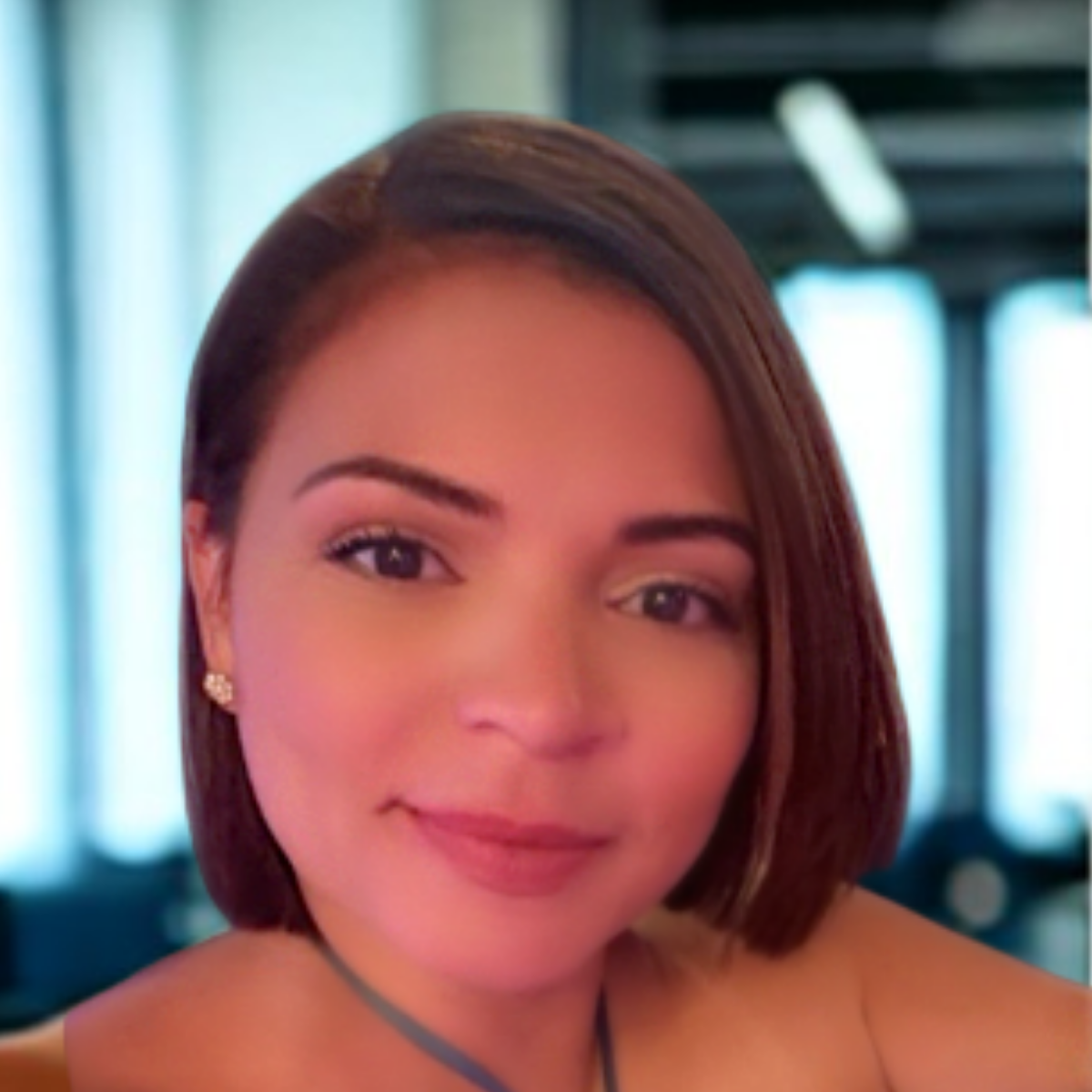 Close-up of a woman with short brown hair and earrings, smiling softly, indoors with bright lighting and blurred background.