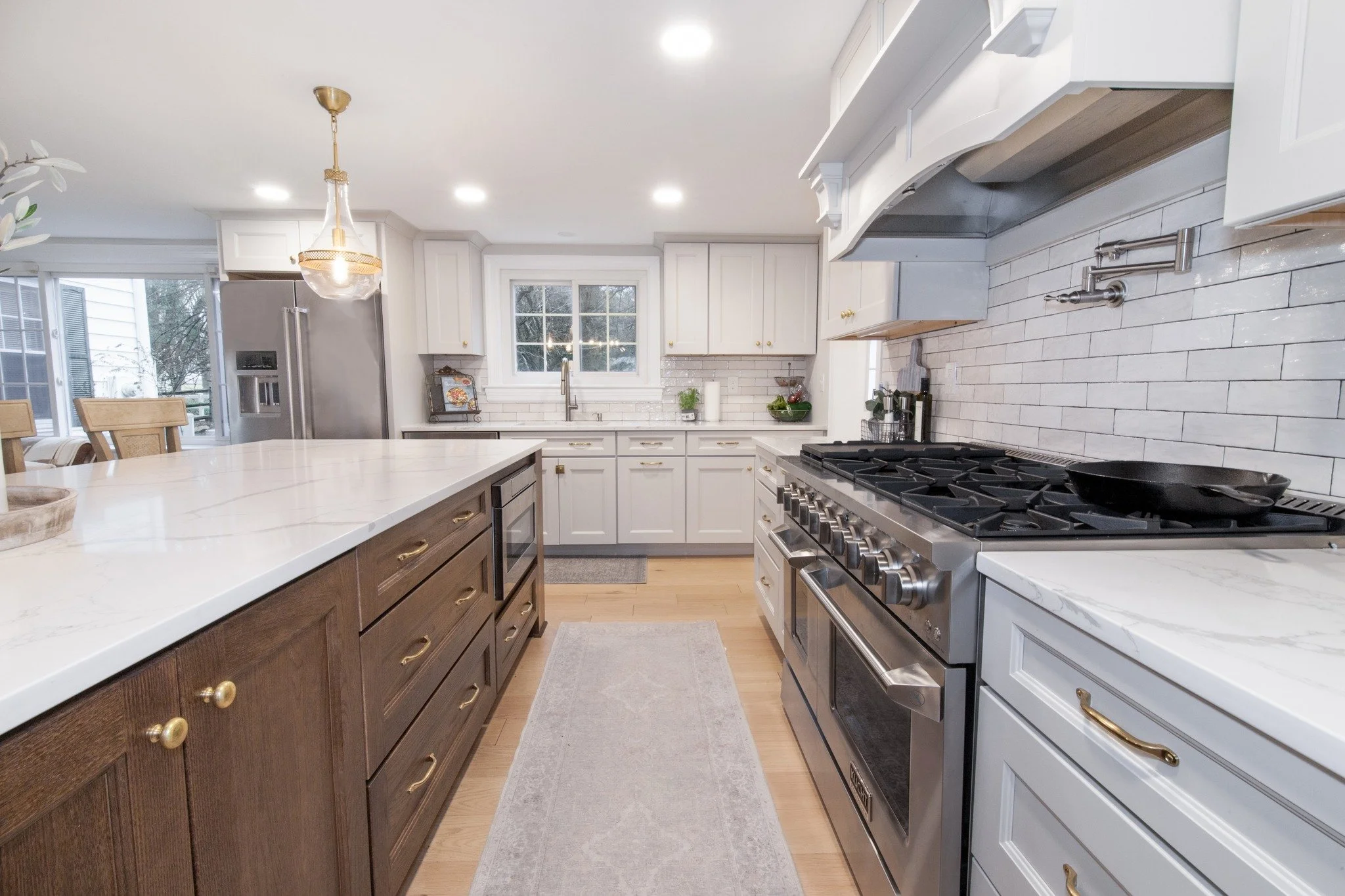 Modern kitchen remodel with white cabinets, stainless steel appliances, and a large island with wooden drawers, a white countertop, and a light gray rug on the wooden floor.