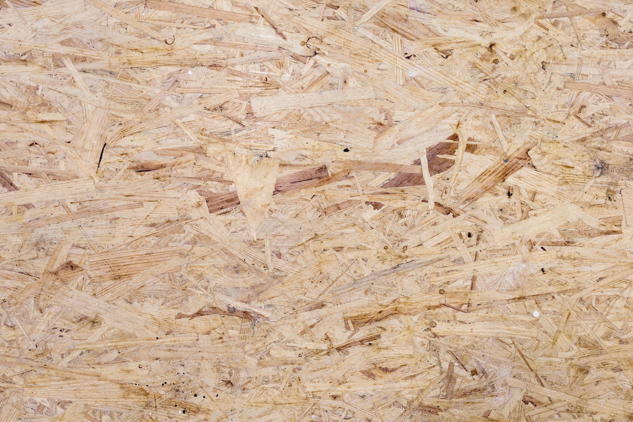 Close-up view of a wooden OSB panel surface with visible wood chips and small black spots.