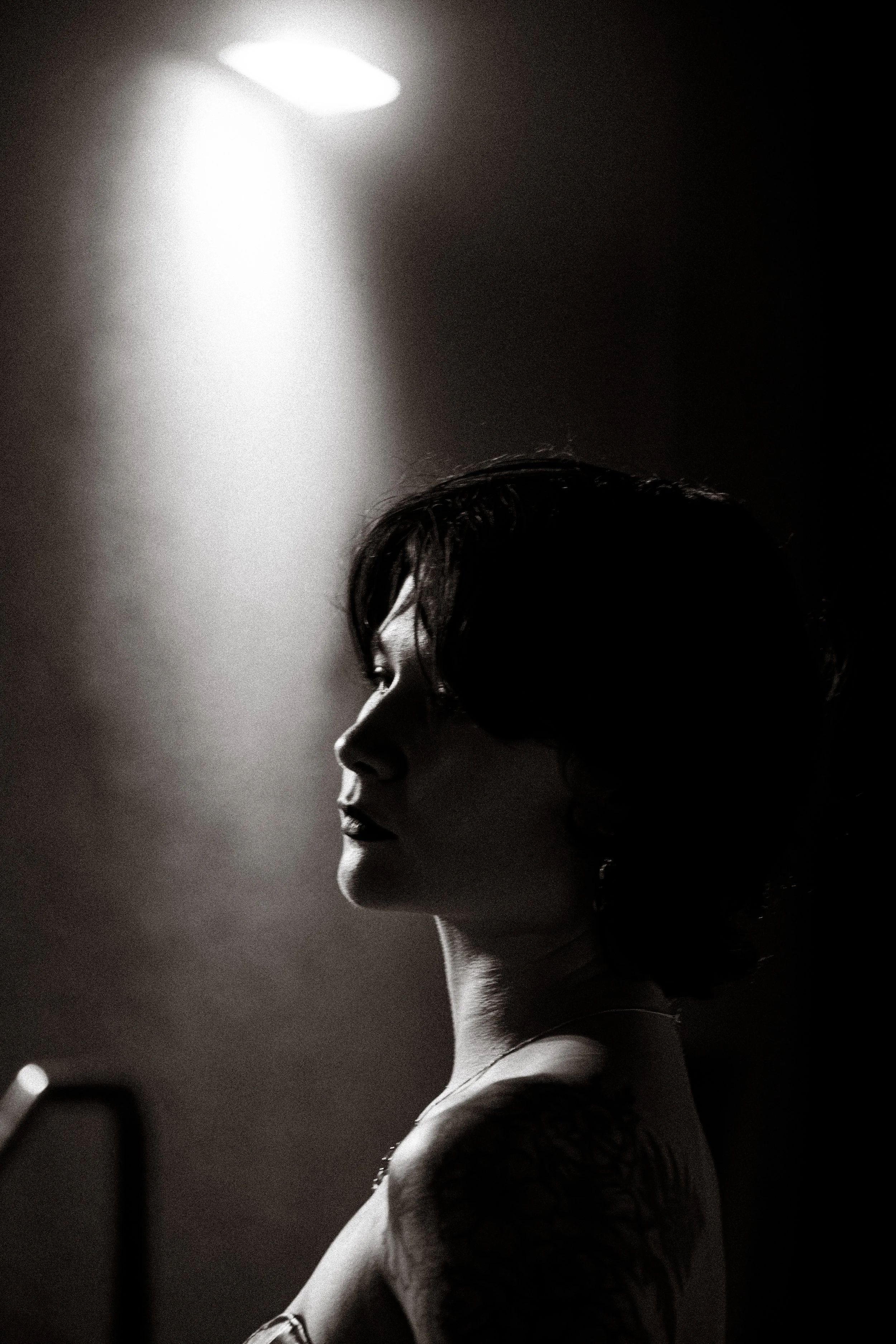 A black-and-white photograph of a woman with short hair, shown in profile, illuminated by a bright light source from above.