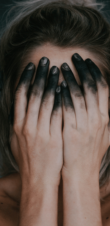 Therapy client covering their face with darkened hands, symbolizing shame, emotional overwhelm, and trauma responses in psychotherapy education.