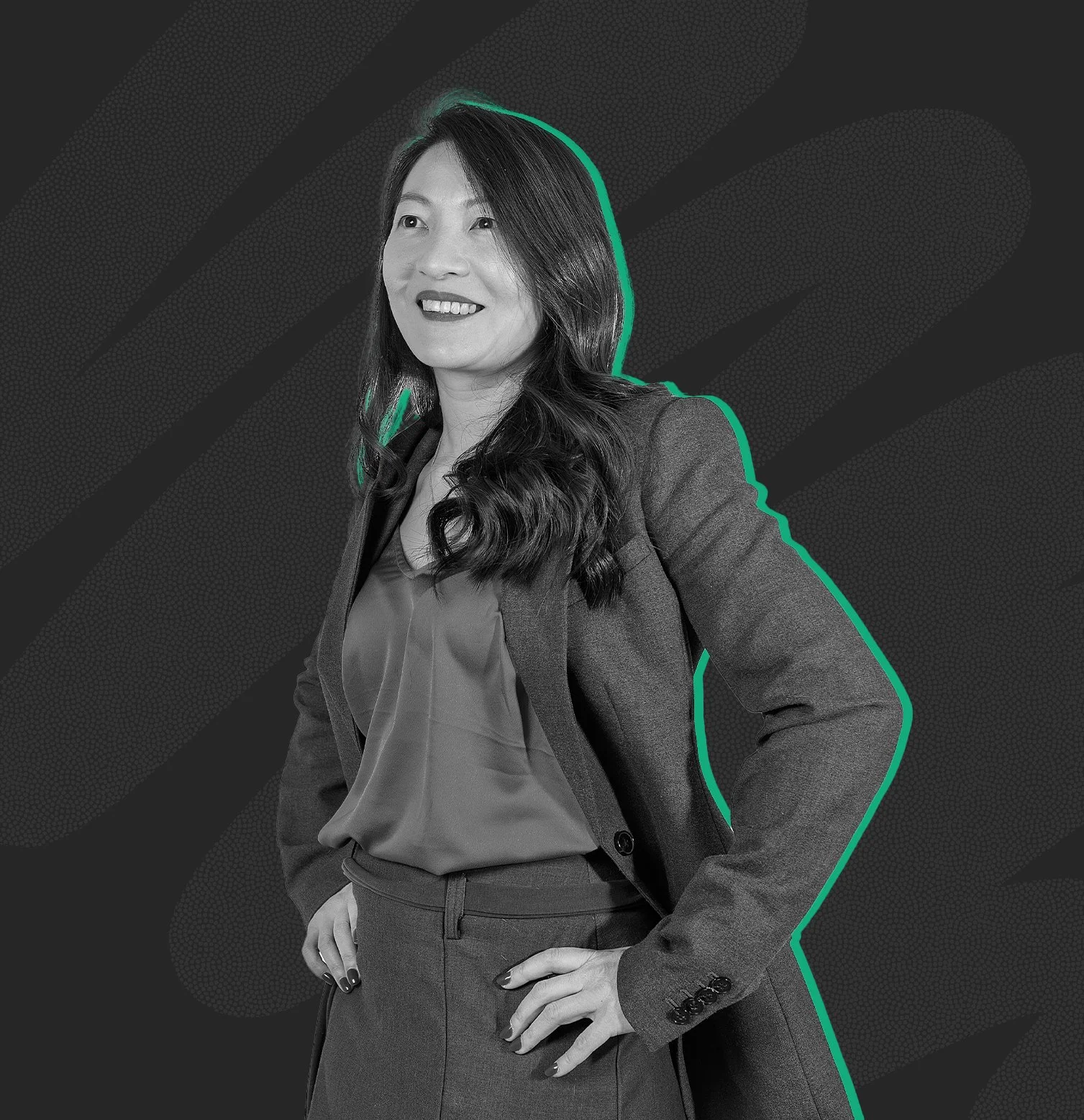 A woman with long brown hair, wearing a black blazer over a blue top, smiling and standing outdoors with a cityscape background.