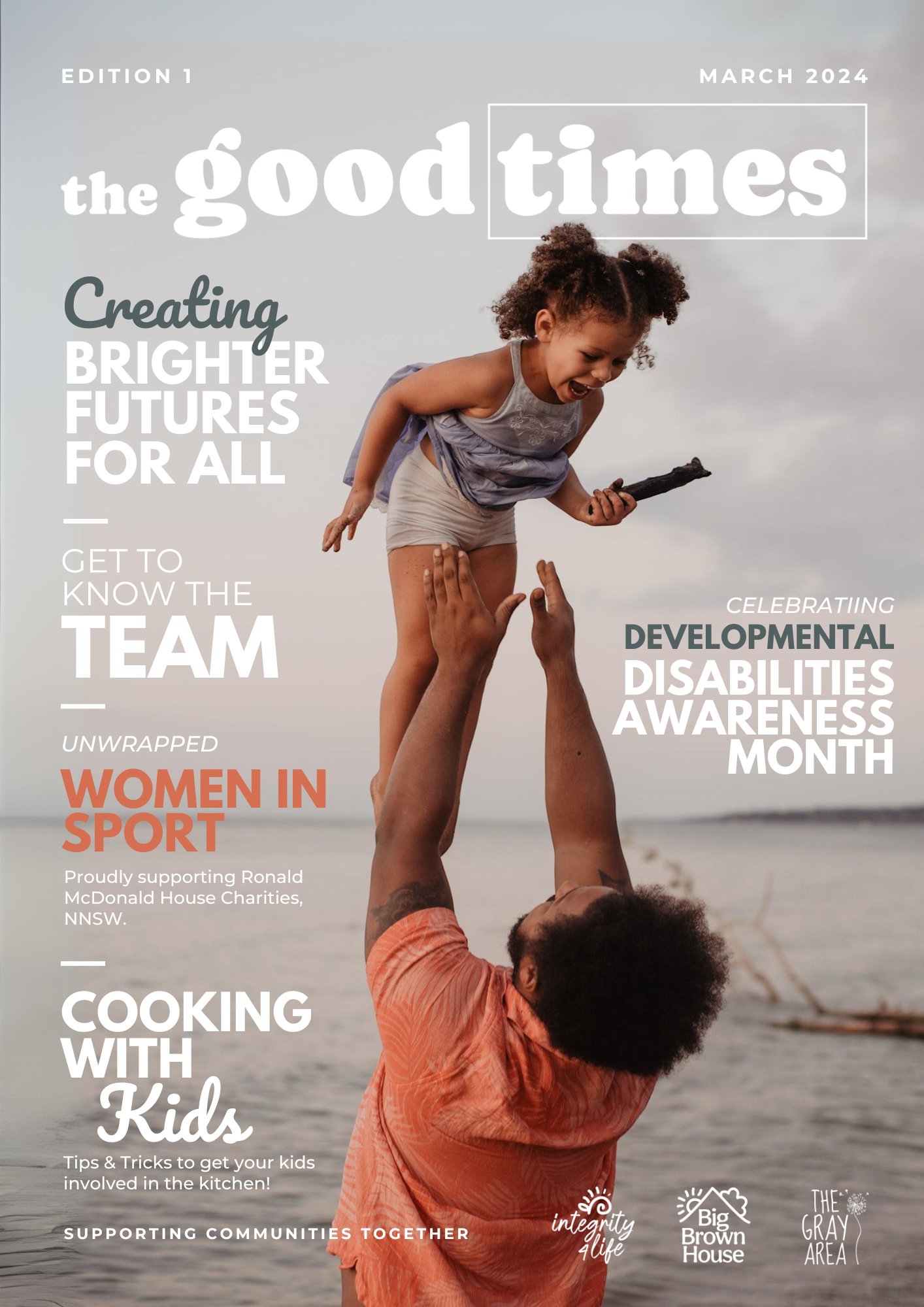 Front cover of a magazine titled 'the good times' March 2024 edition. The cover features a person with curly hair lifting a smiling young girl with curly hair in the air at the beach. The girl is holding a stick, and the background shows the ocean and sky.