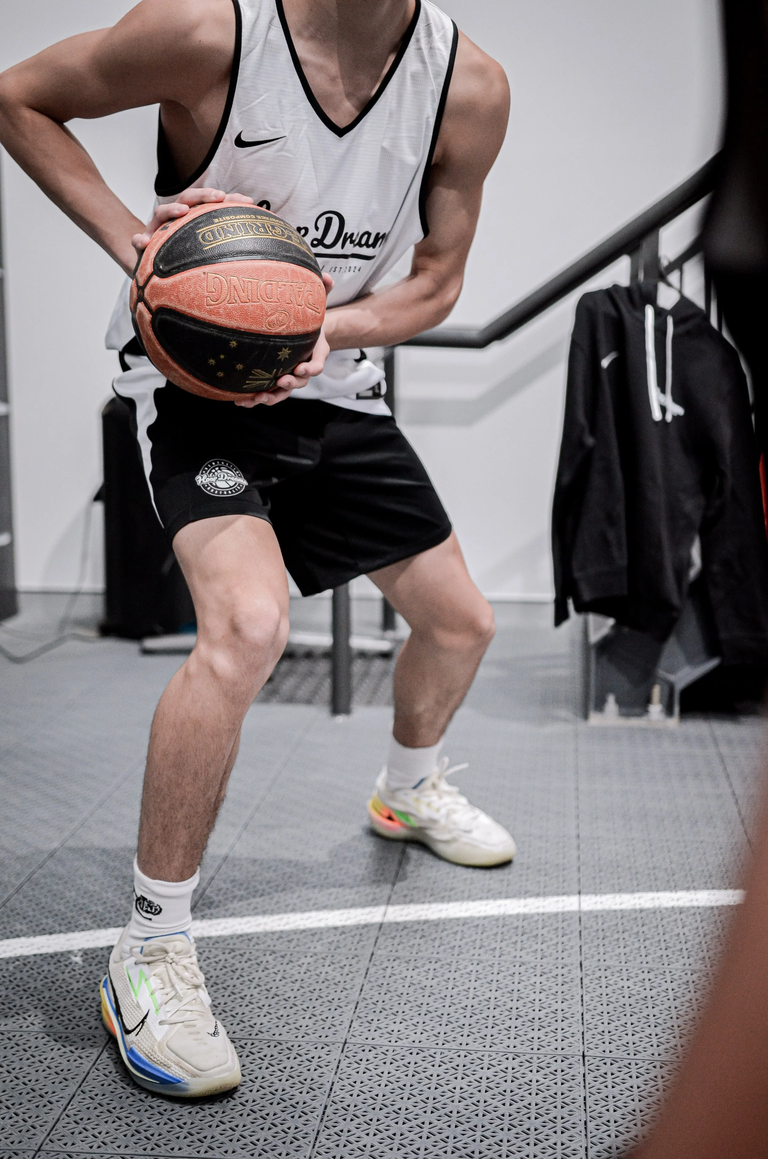 A person in a basketball jersey and shorts holding a basketball, positioned in a basketball stance on a gym floor.