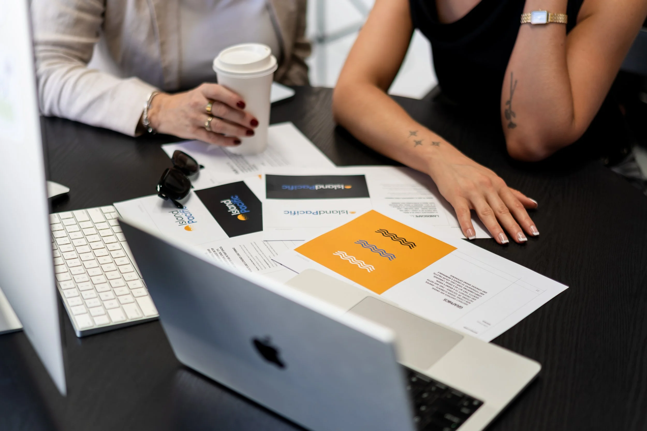 Two people sitting at a desk with documents, a computer, and a cup of coffee.