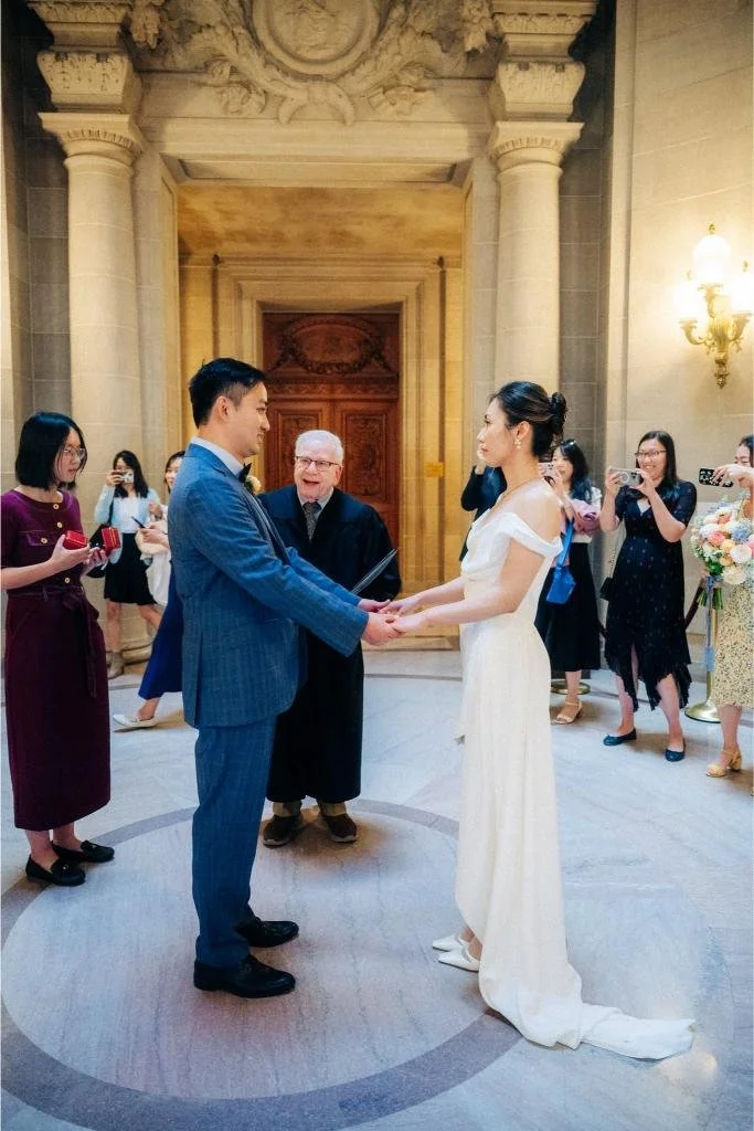Bride and groom facing each other and holding hands as the officiant looks on during their ceremony.