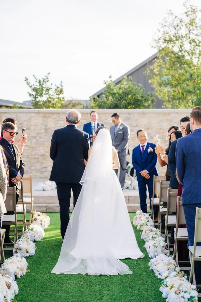 Bride and her father walking down the wedding aisle photographed from behind