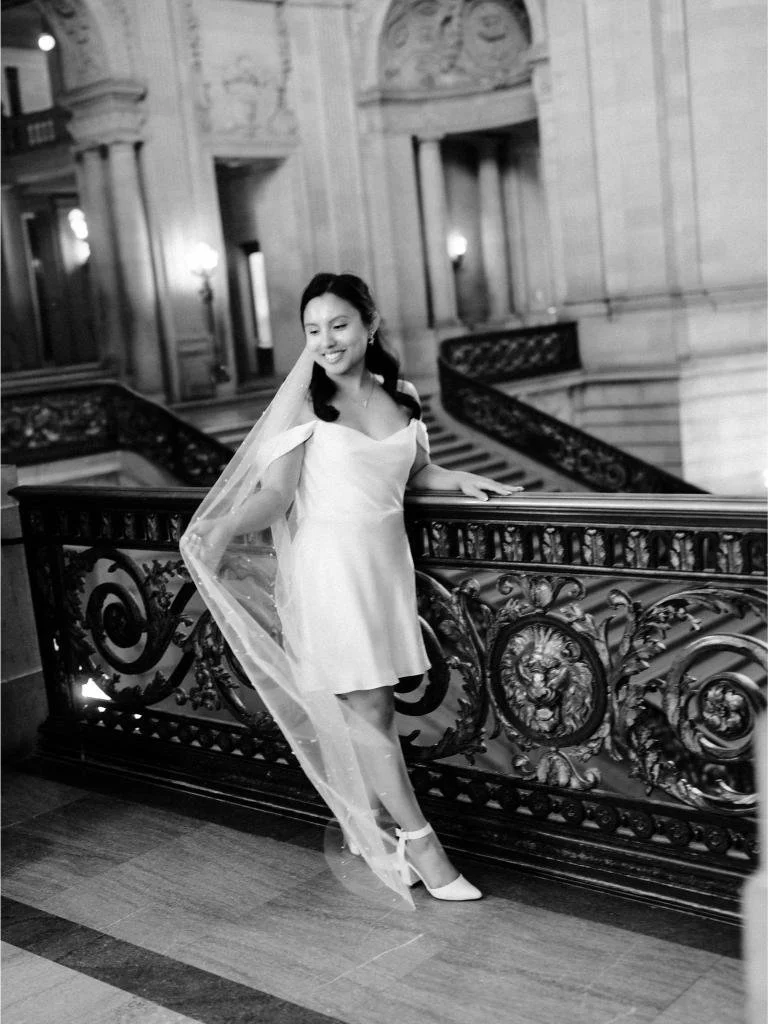 Bride standing beside a railing at San Francisco City Hall while holding her veil