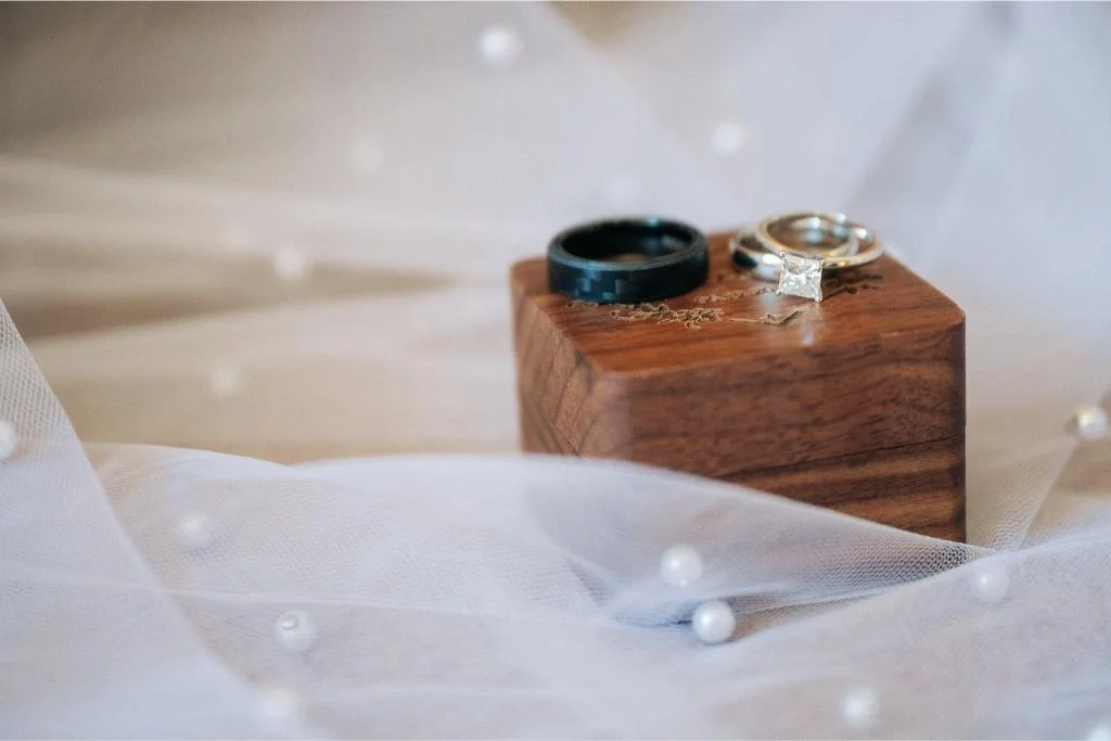 Wedding rings displayed on a brown wooden box beside the bride's veil