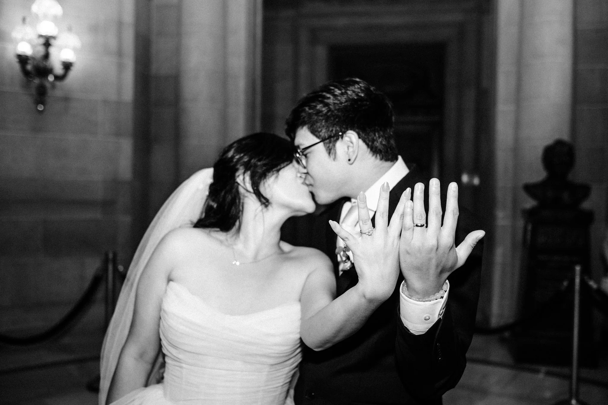Newlyweds kissing and showing wedding rings at San Francisco City Hall